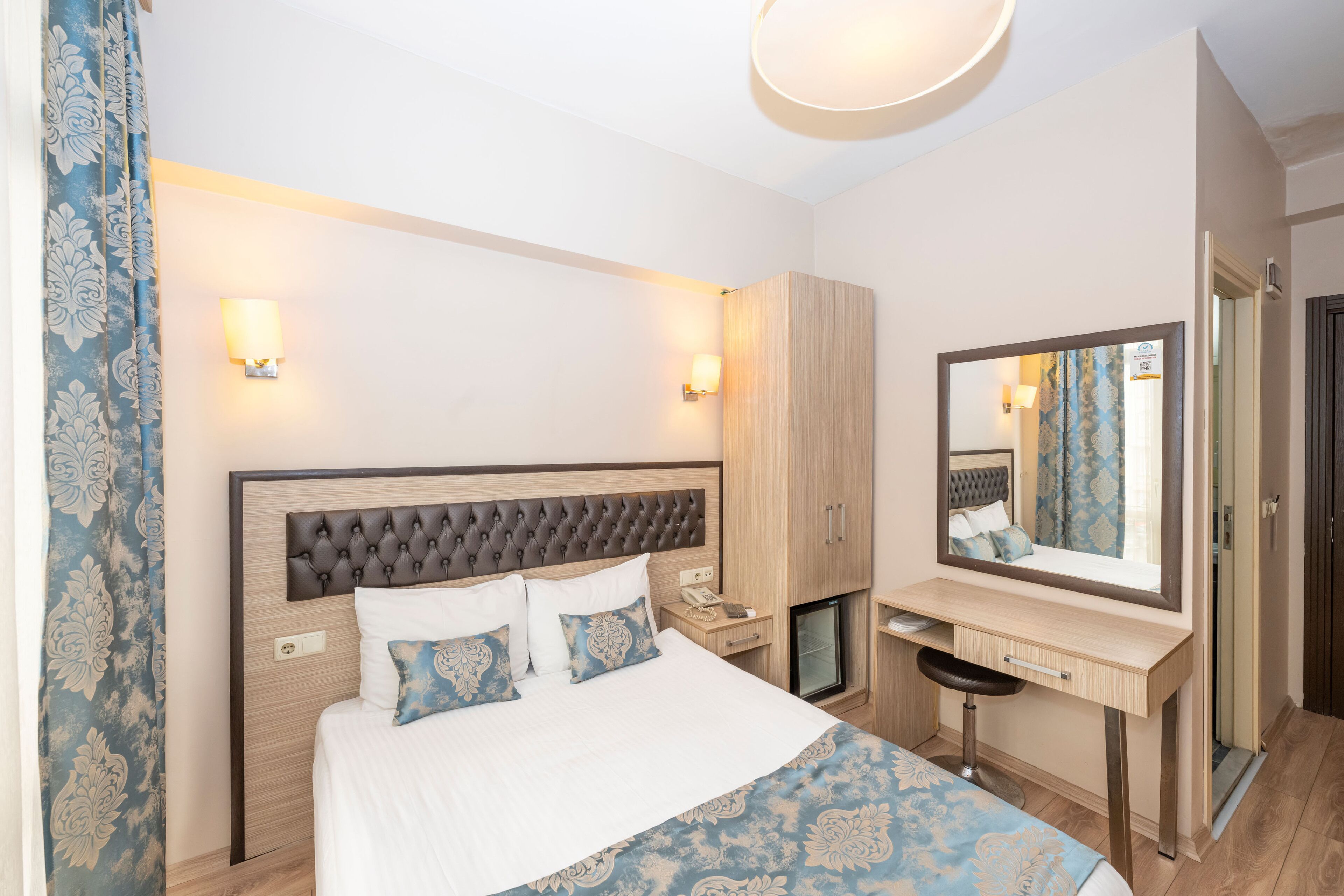 A bedroom with a bed, bedside table, mirror, wardrobe, and a small desk.