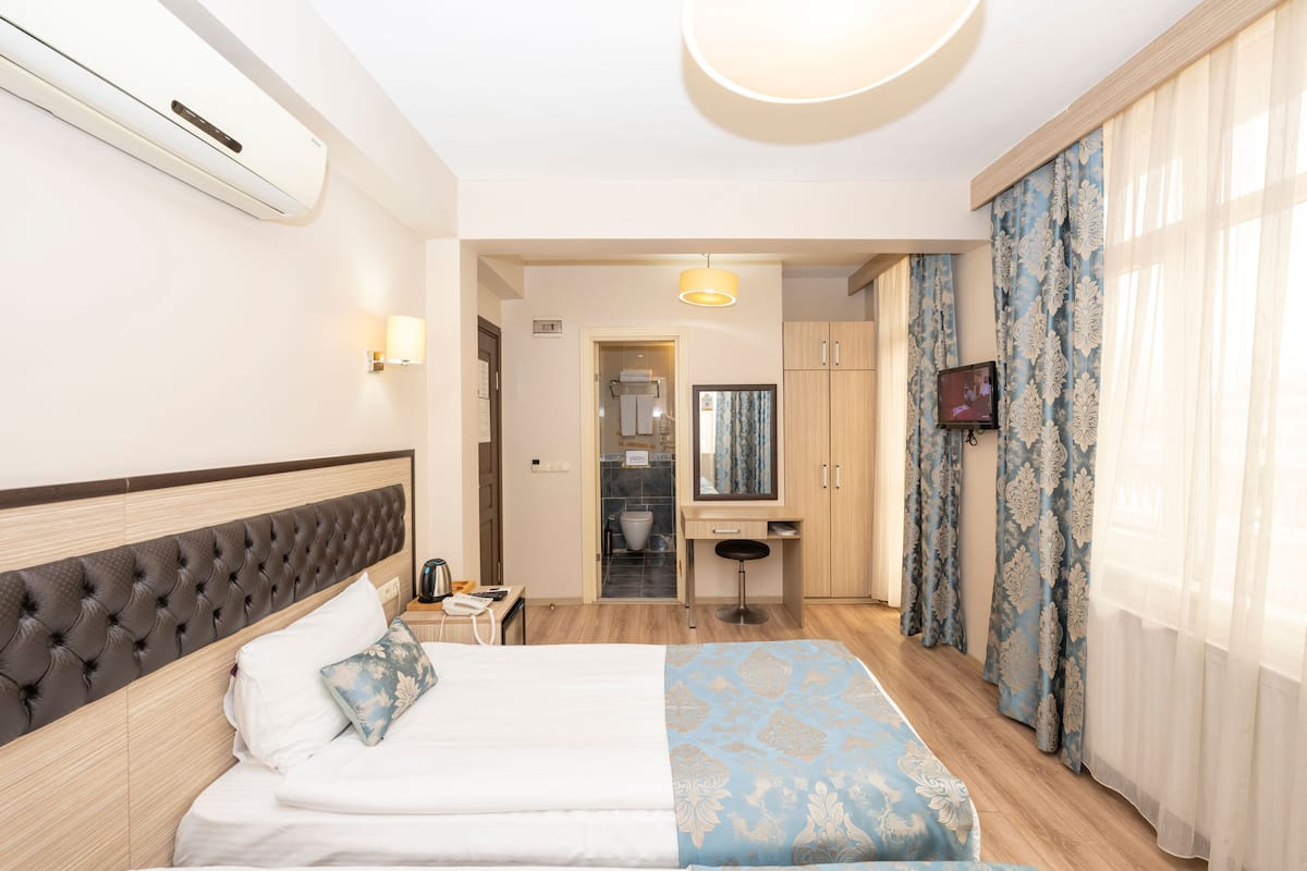 Une chambre d’hôtel avec un lit, un bureau, un miroir, une télévision et une salle de bain visible à travers une porte ouverte.