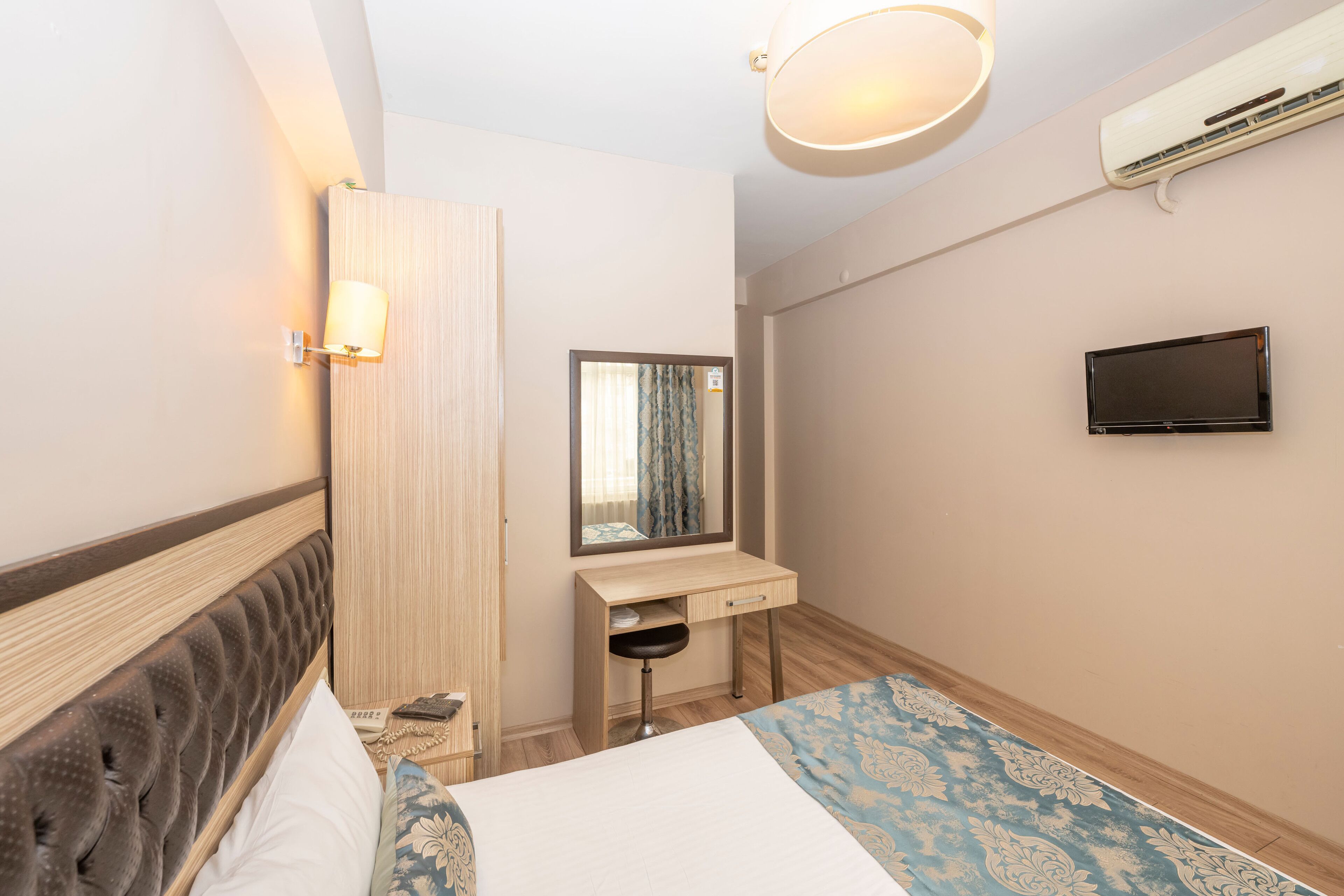 Ett hotellrum med en säng, ett skrivbord, en spegel, en TV och en luftkonditioneringsanläggning.
