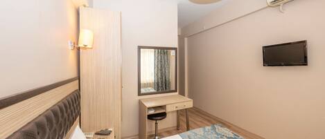 A hotel room with a bed, a desk, a mirror, a TV, and an air conditioning unit.