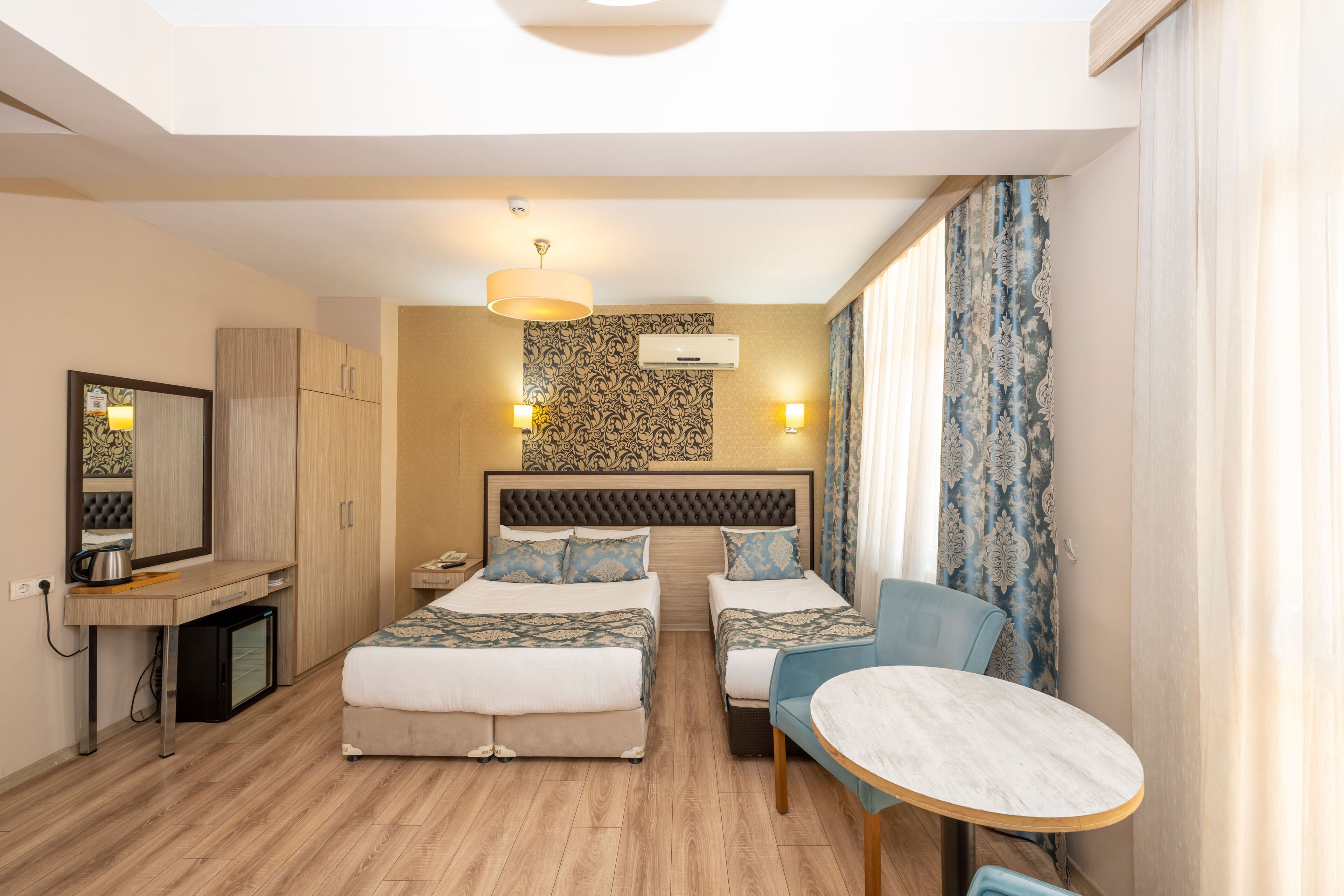 A hotel room with two beds, a desk, a chair, a small table, and a mirror.