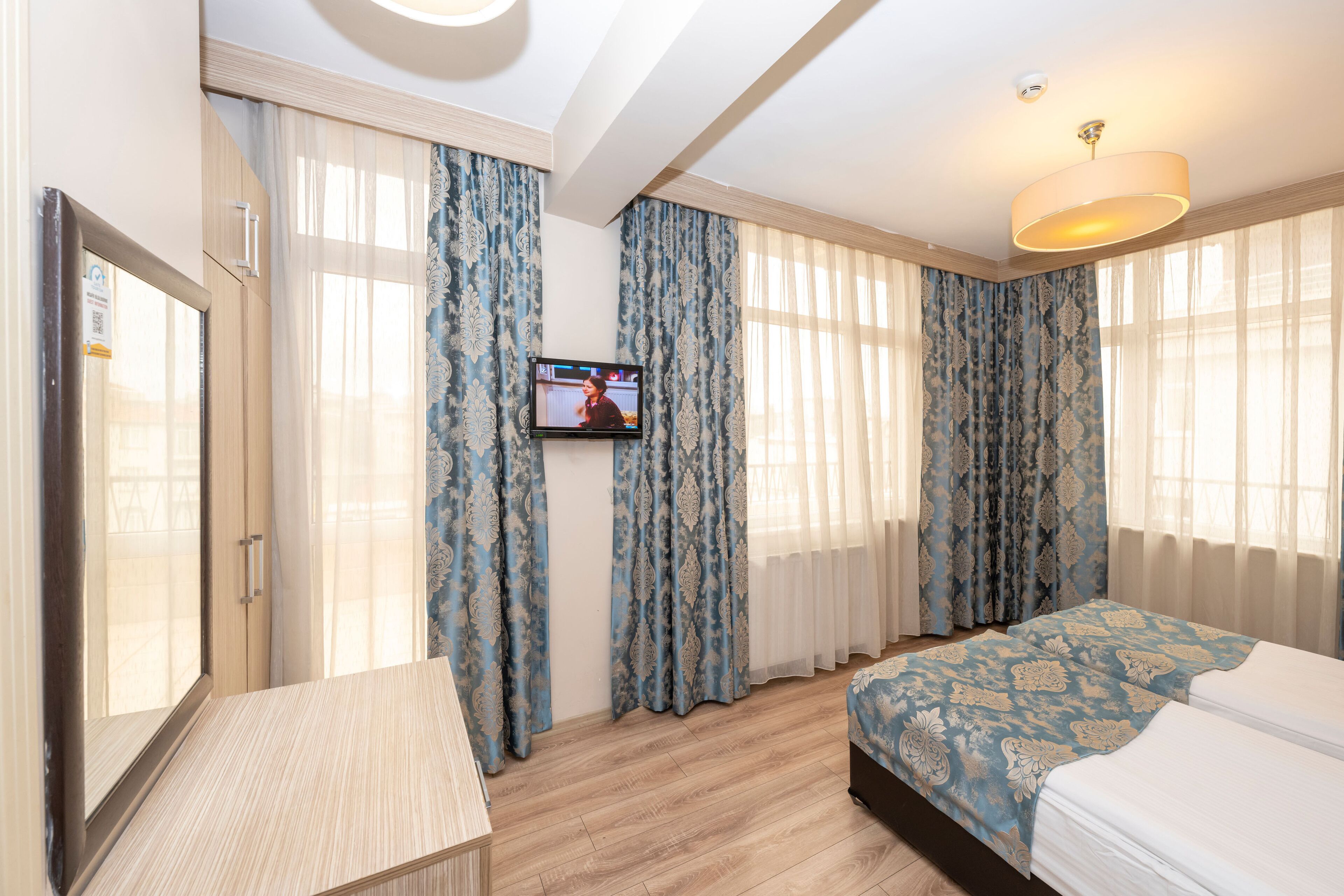 Habitación de hotel con cama, escritorio, televisor y cortinas.