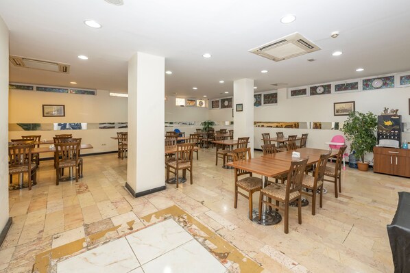 Un vaste espace dédié à la salle à manger, avec de nombreuses tables et chaises en bois, un pilier central et une plante en pot.