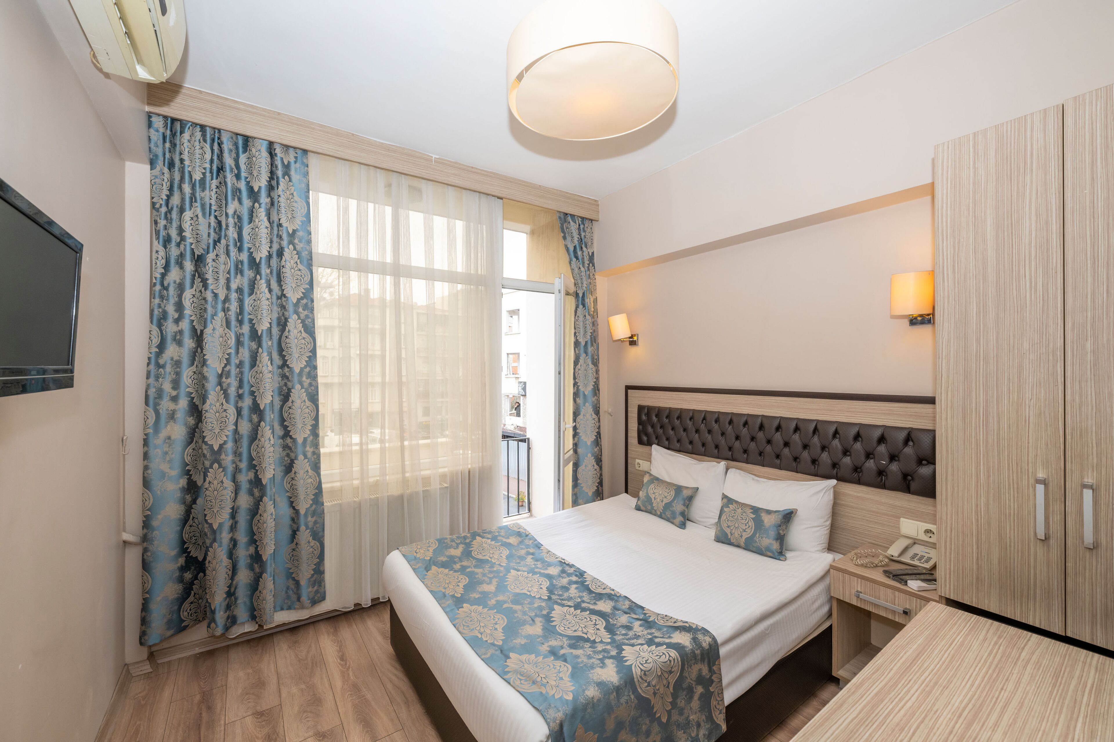 A hotel room with a large bed, a bedside table with a lamp, a wardrobe, and a television on the wall.