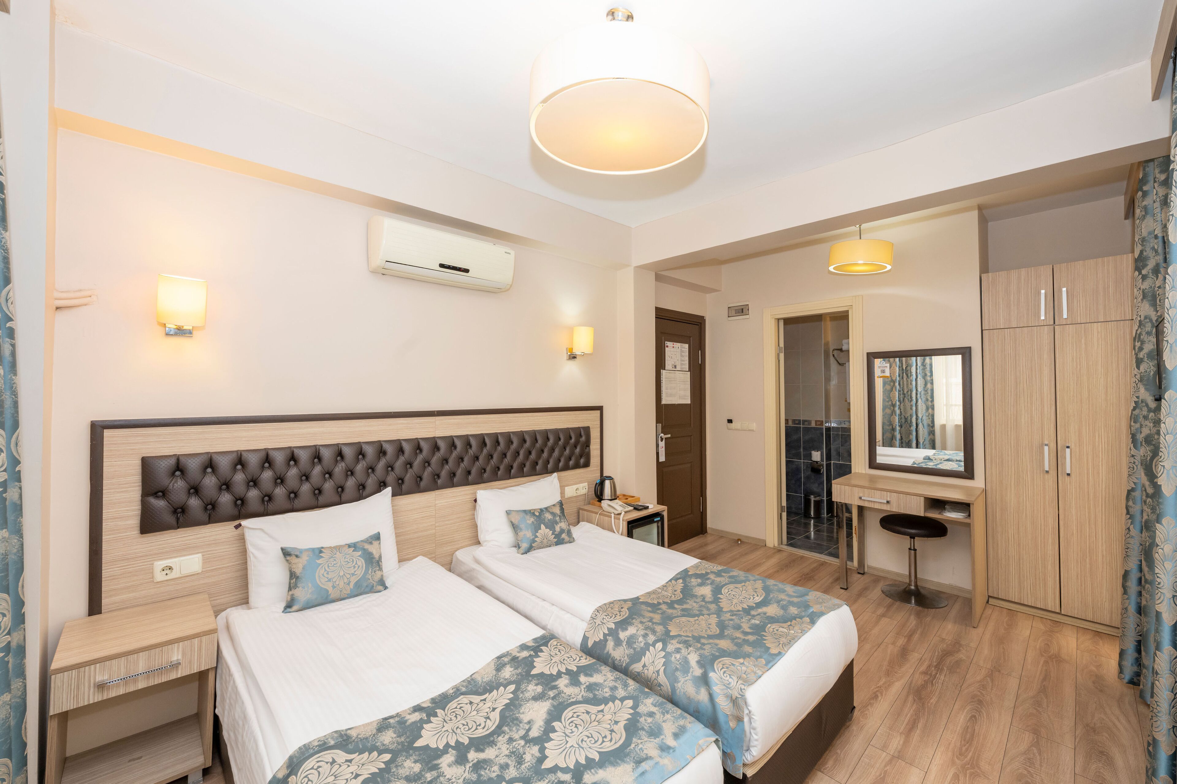 A hotel room with two beds, a desk, a mirror, and a wardrobe.
