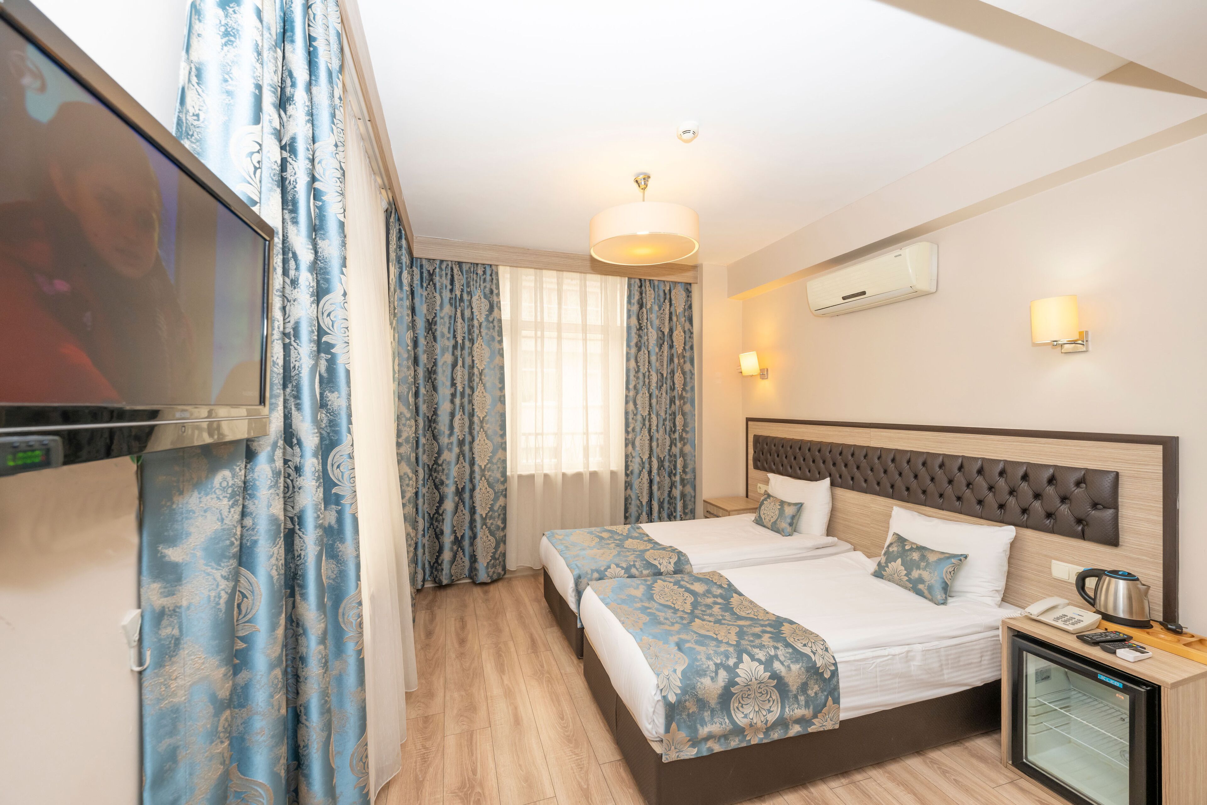A hotel room with two beds, a TV, a minibar, and a window with curtains.