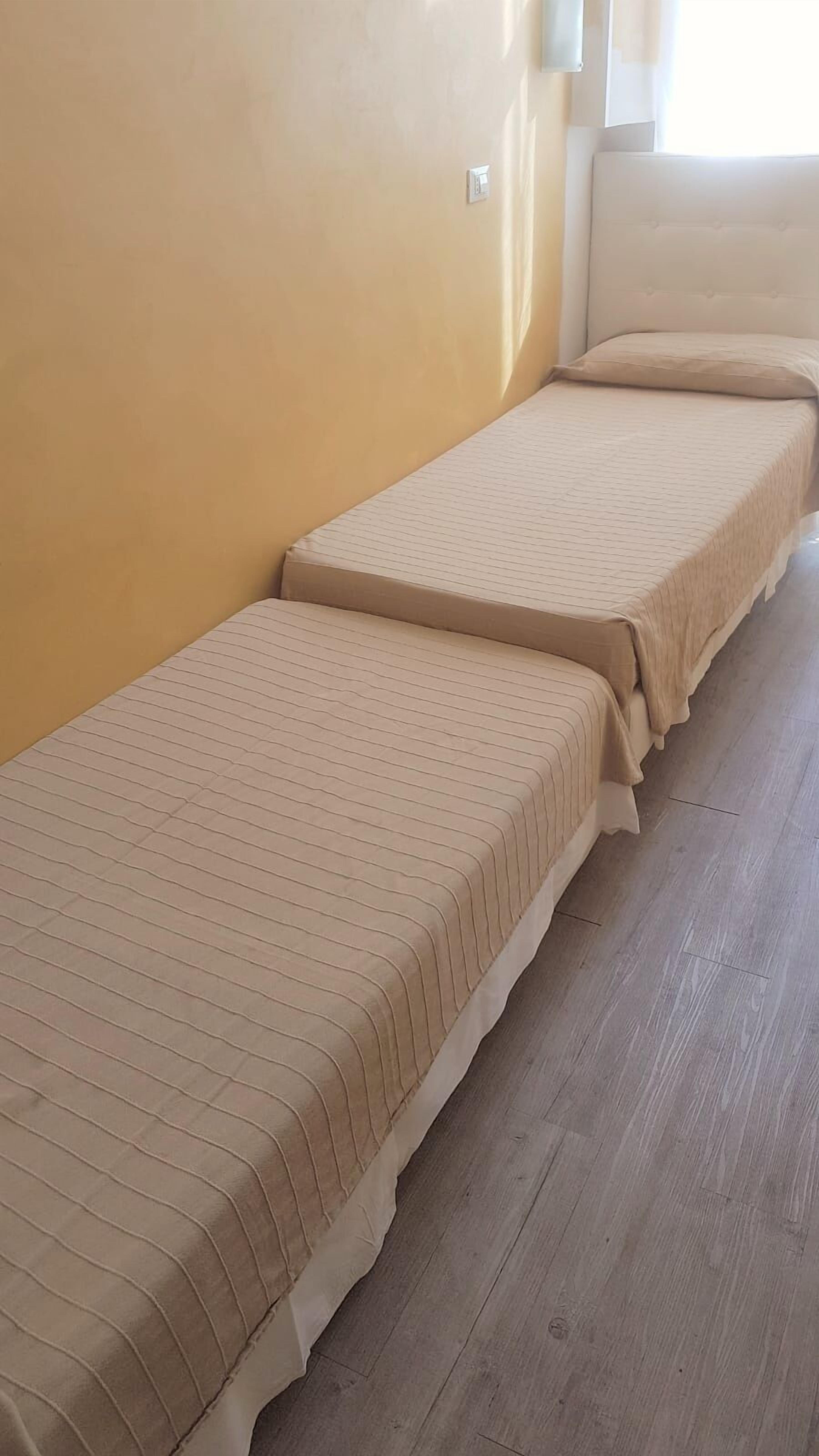 Two single beds with striped bedding in a room with wooden flooring and yellow walls.