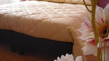 A bed with a tufted headboard, a beige quilted bedspread, and a wooden floor.