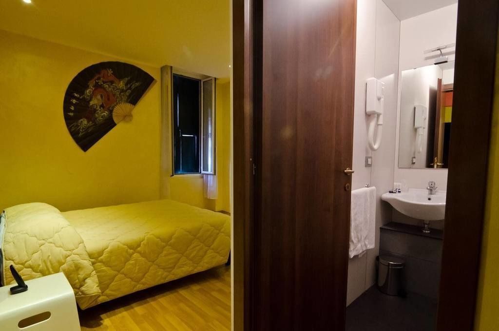 A room with a bed, a fan, a window, and a bathroom with a sink and mirror.