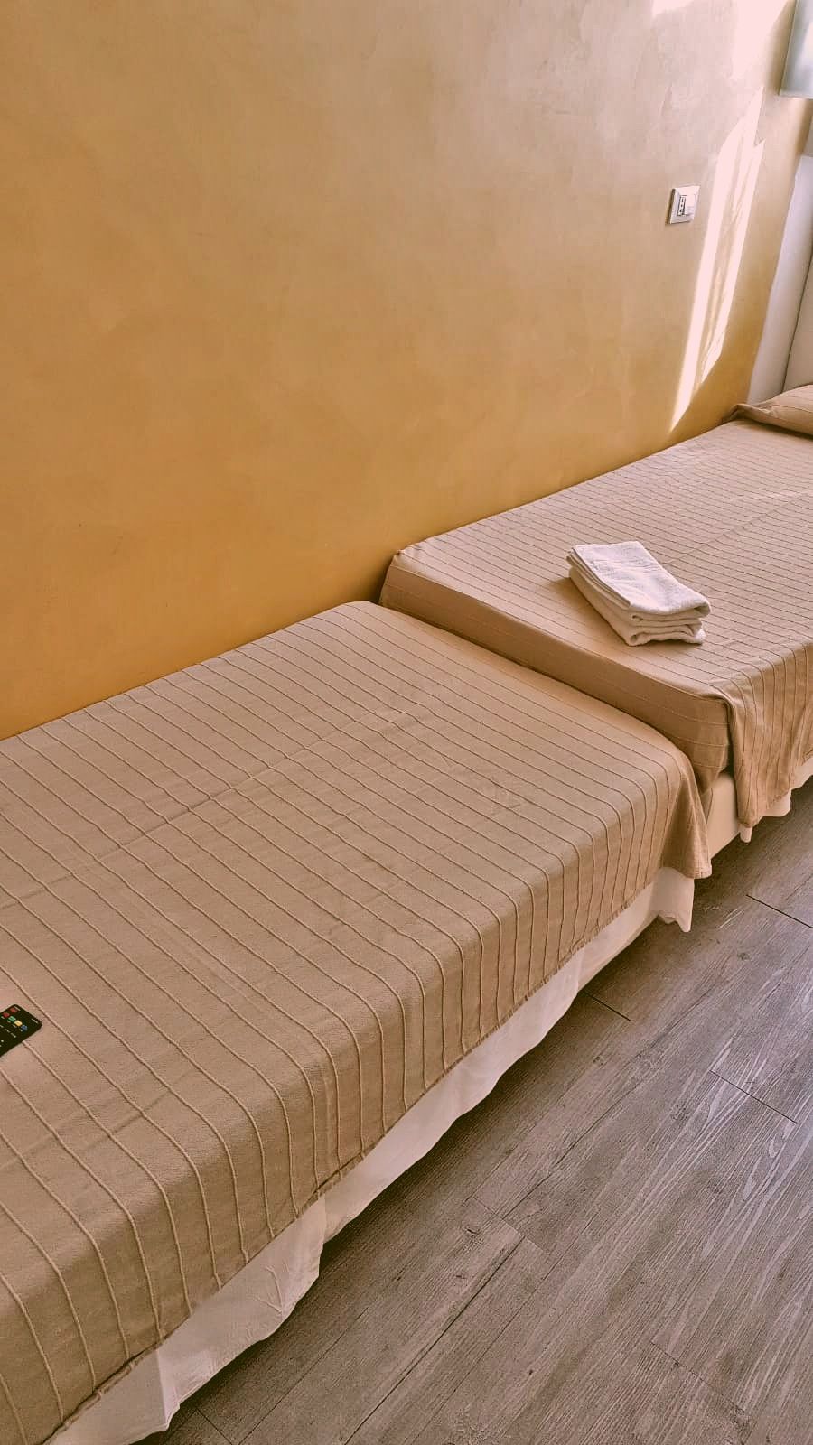 Zwei Einzelbetten mit gestreifter Bettwäsche in einem Zimmer mit Holzboden und einer schlichten gelben Wand.