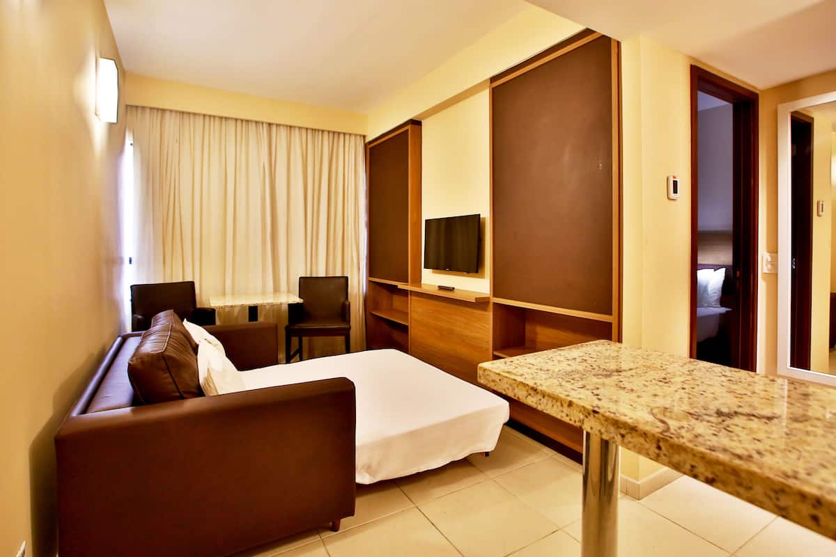 Une chambre d’hôtel comprenant un lit, un canapé, une petite table, une télévision et une porte donnant sur une autre pièce.