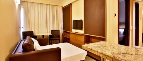 A hotel room with a bed, a sofa, a small table, a TV, and a door leading to another room.