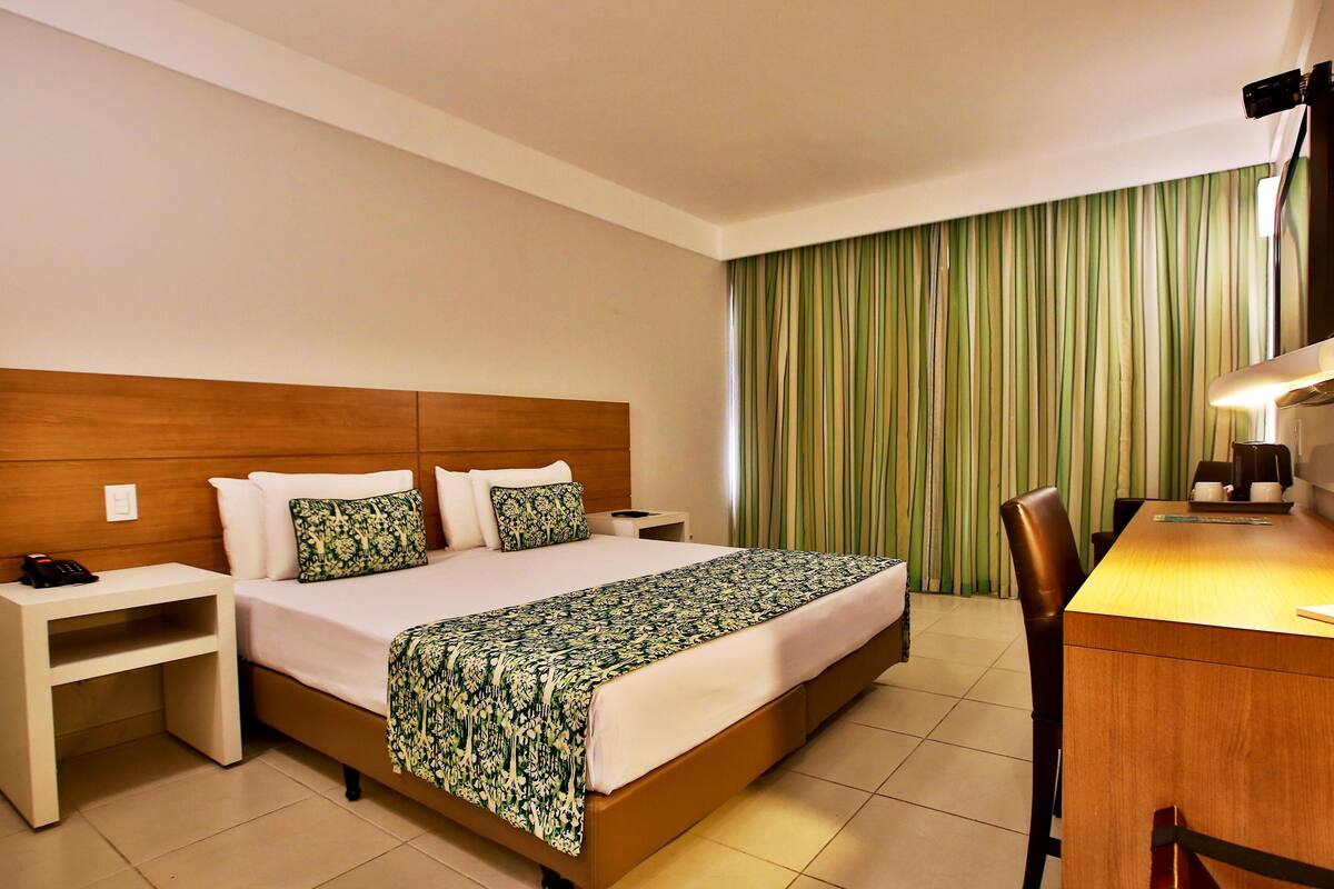 Ein Hotelzimmer mit Bett, Schreibtisch, Stuhl und Vorhang.