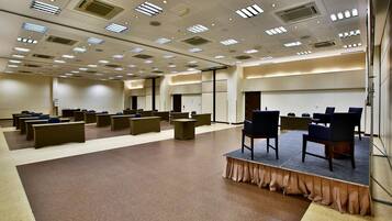 Un salón de conferencias con hileras de sillas, un escenario y una pantalla grande.