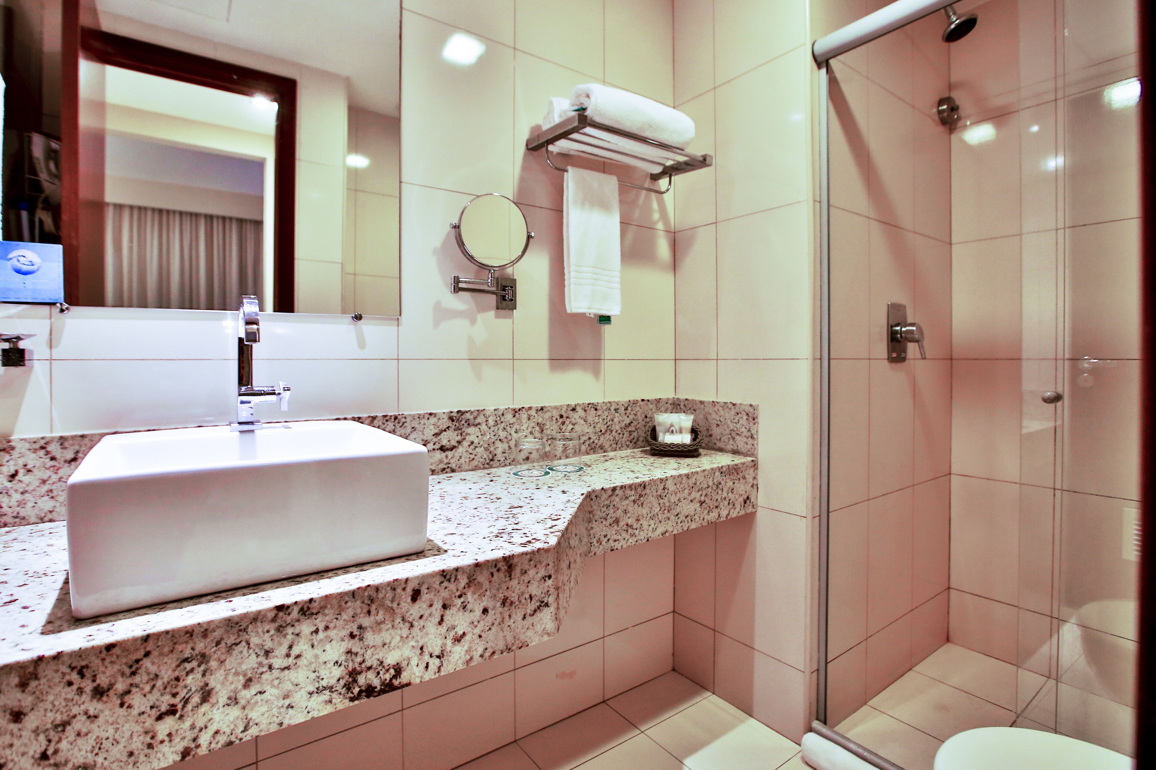 A modern bathroom with a granite countertop, a white sink, a glass-enclosed shower, and a mirror with a towel rack.