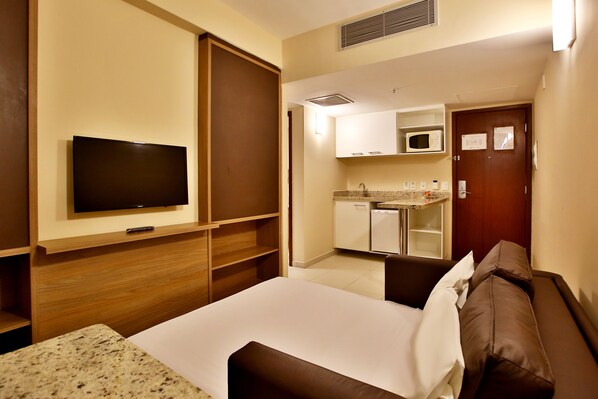 Una habitación de hotel con cama, televisor, kitchenette y una puerta.