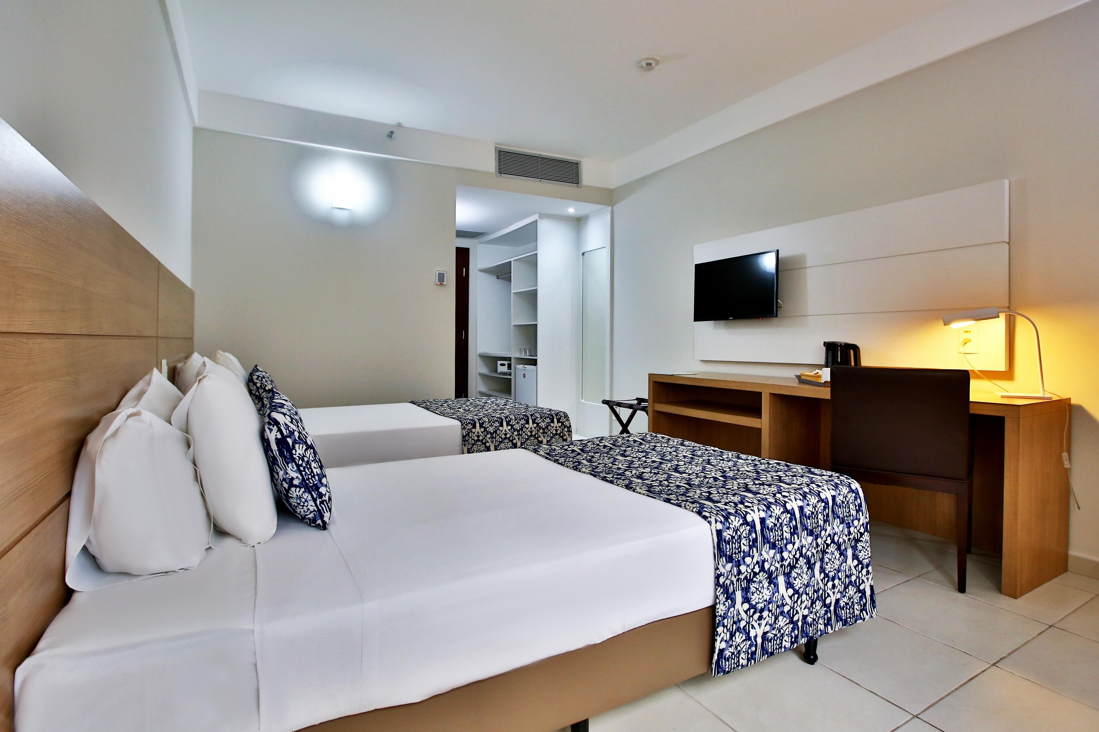 Habitación de hotel con cama, escritorio, silla, televisor y armario.