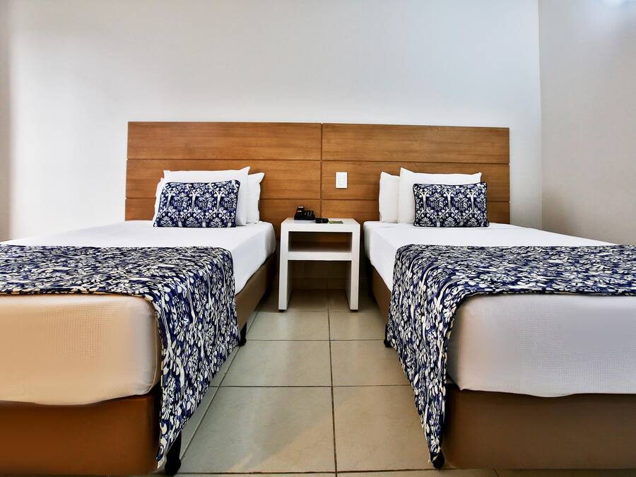 A hotel room with two beds, each with a patterned bedspread, a wooden headboard, and a small bedside table with a lamp.