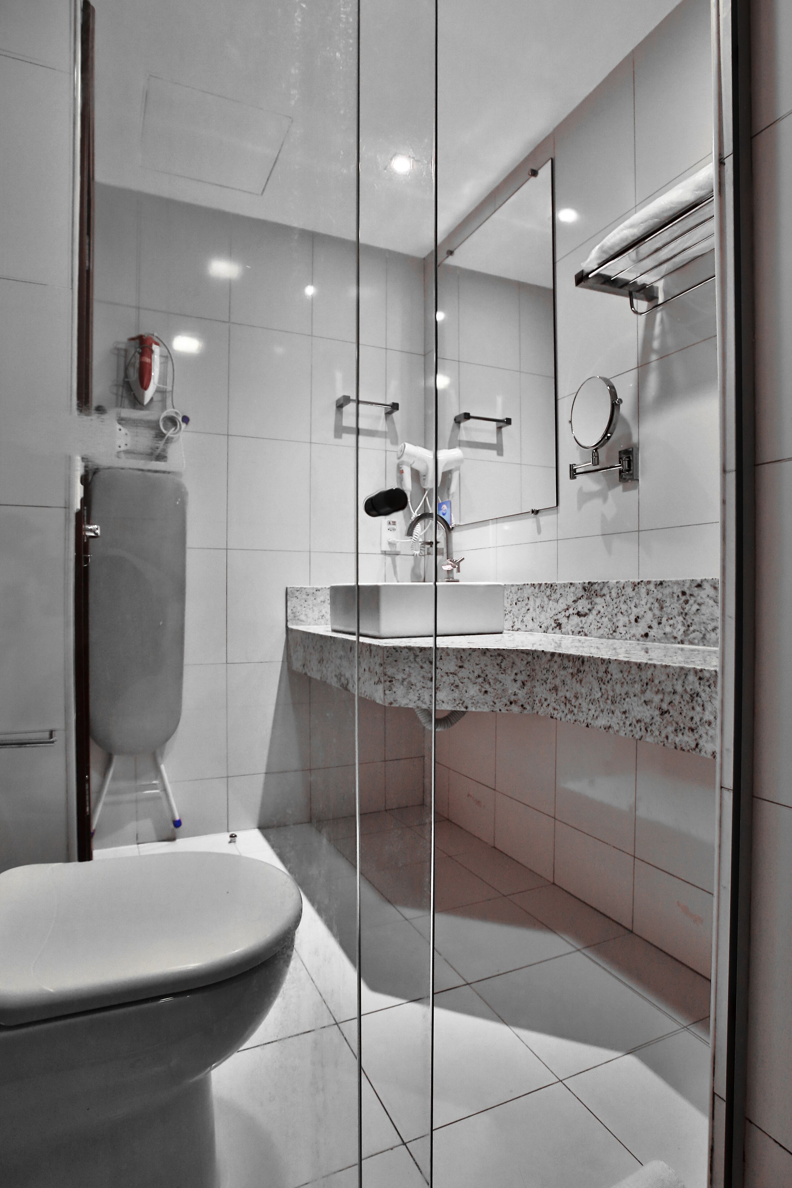 A modern bathroom with a glass shower enclosure, a toilet, a sink with a granite countertop, and a mirror with a towel rack.