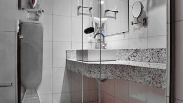 A modern bathroom with a glass shower enclosure, a toilet, a sink with a granite countertop, and a mirror with a towel rack.