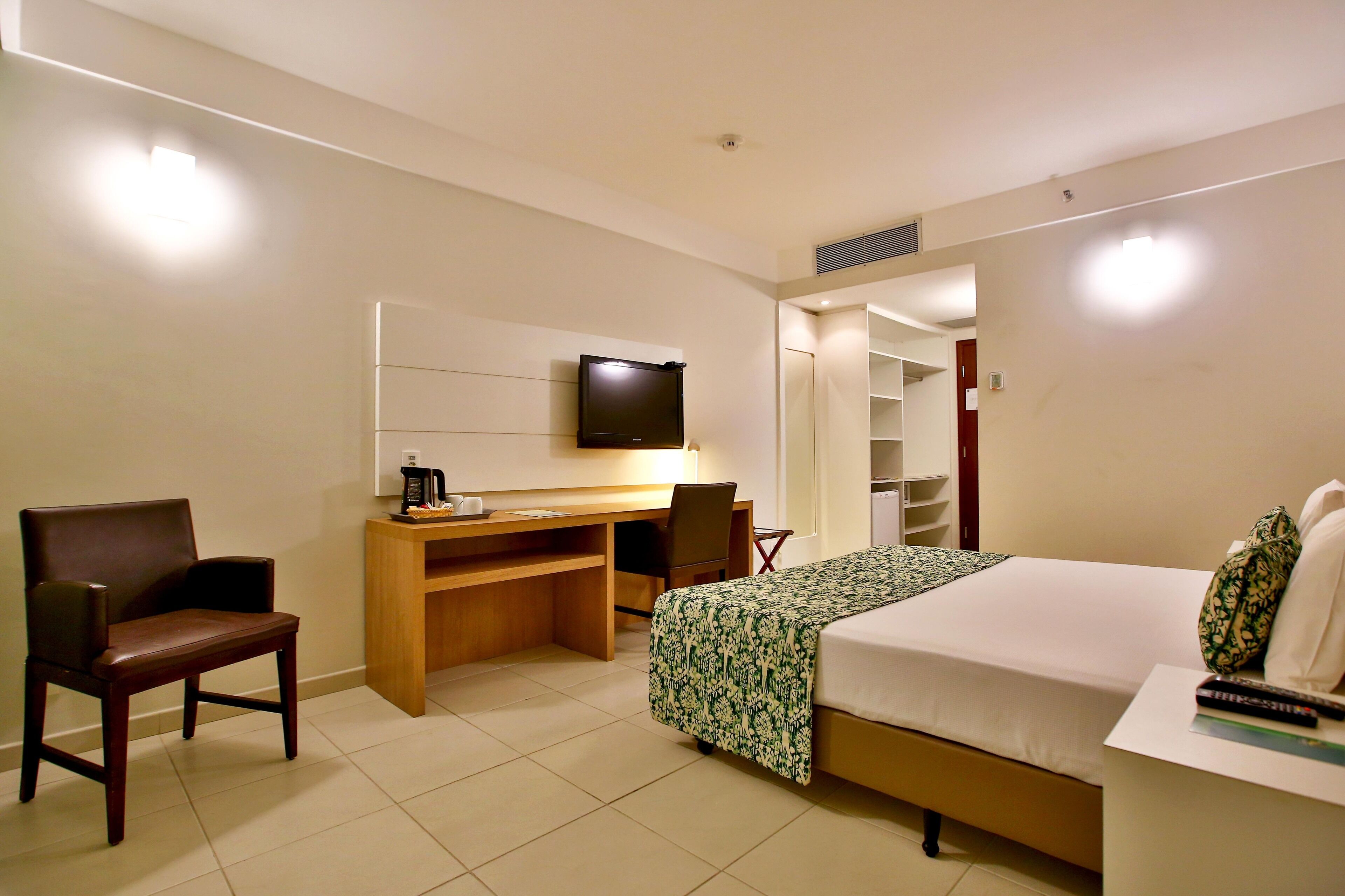 A hotel room with a bed, a desk with a chair, a television, and a wardrobe.