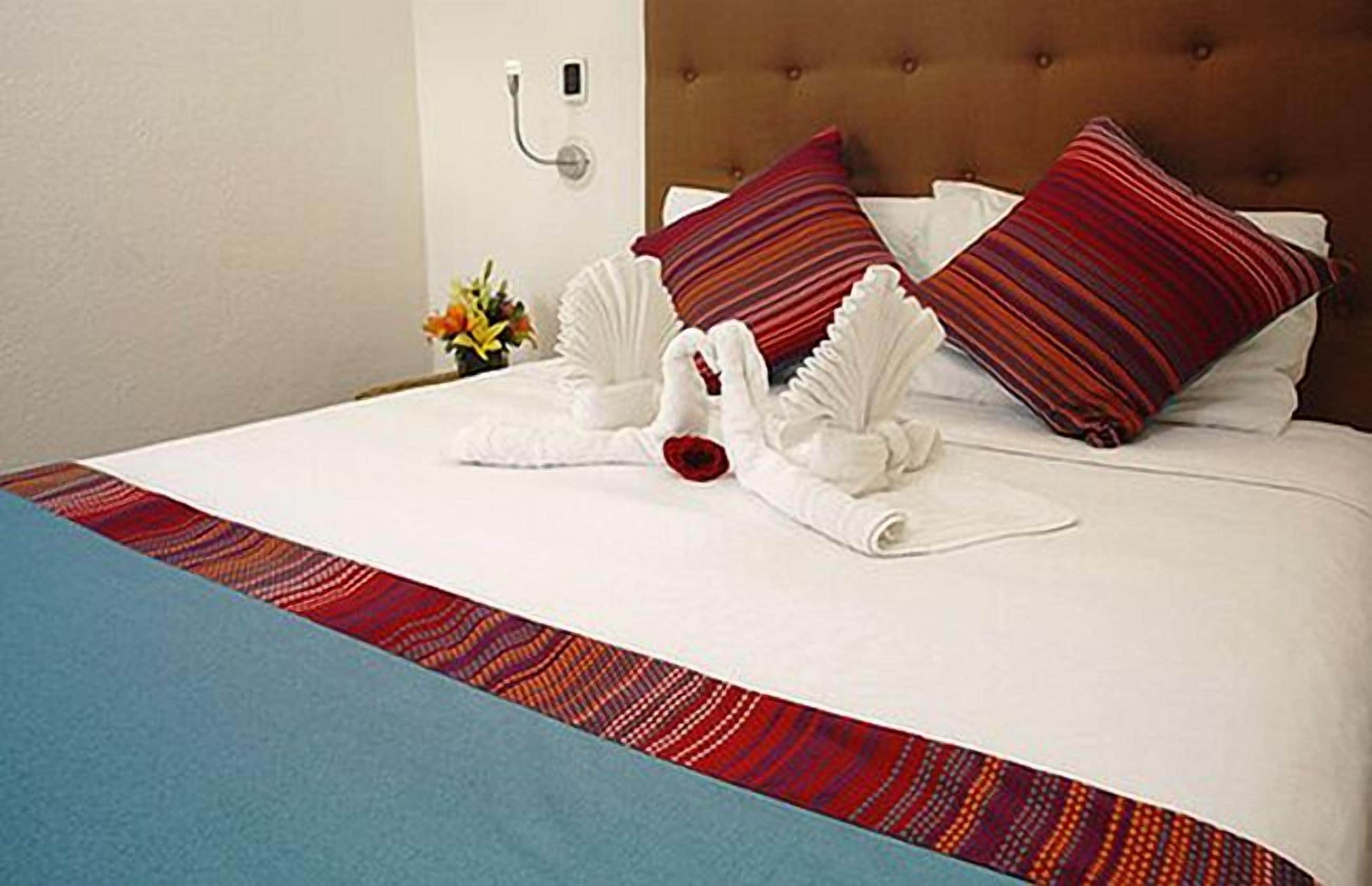 A hotel room with a neatly made bed, pillows, and a decorative towel arrangement.