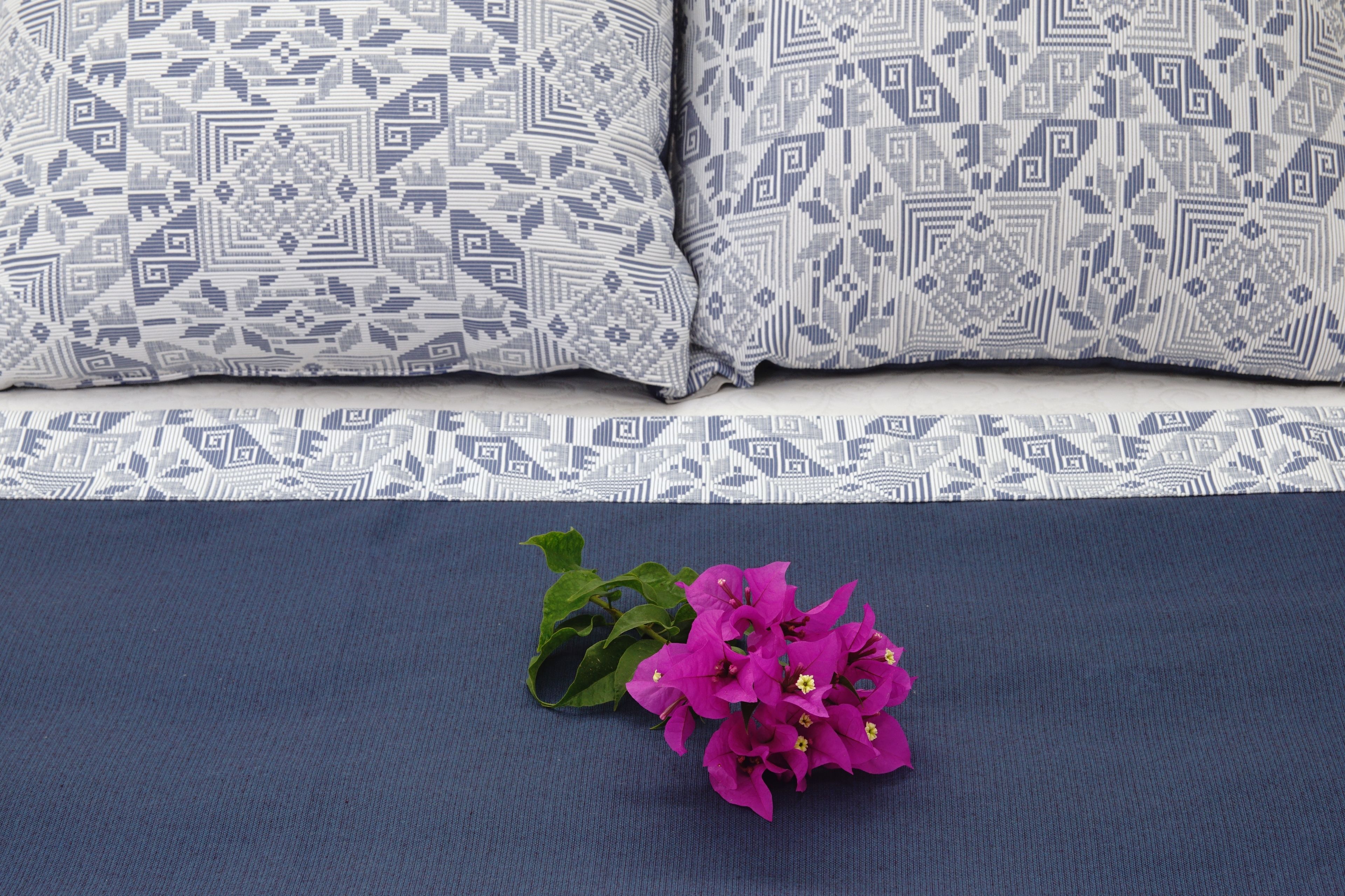 Una cama con ropa de cama estampada y un ramo de flores púrpuras sobre el edredón.