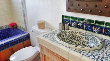 A bathroom with a white toilet, a blue and white tiled shower area, a wooden cabinet, and a sink with a floral tile backsplash.