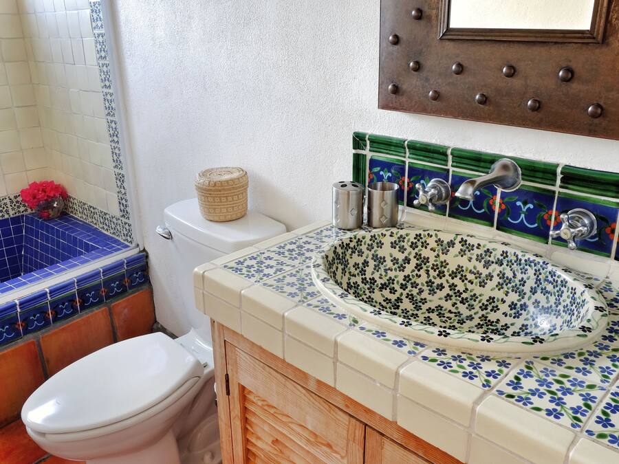 A bathroom with a white toilet, a blue and white tiled shower area, a wooden cabinet, and a sink with a floral tile backsplash.