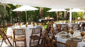 Un'area pranzo all'aperto con tavoli apparecchiati per un pasto, circondata da vegetazione lussureggiante e palme.