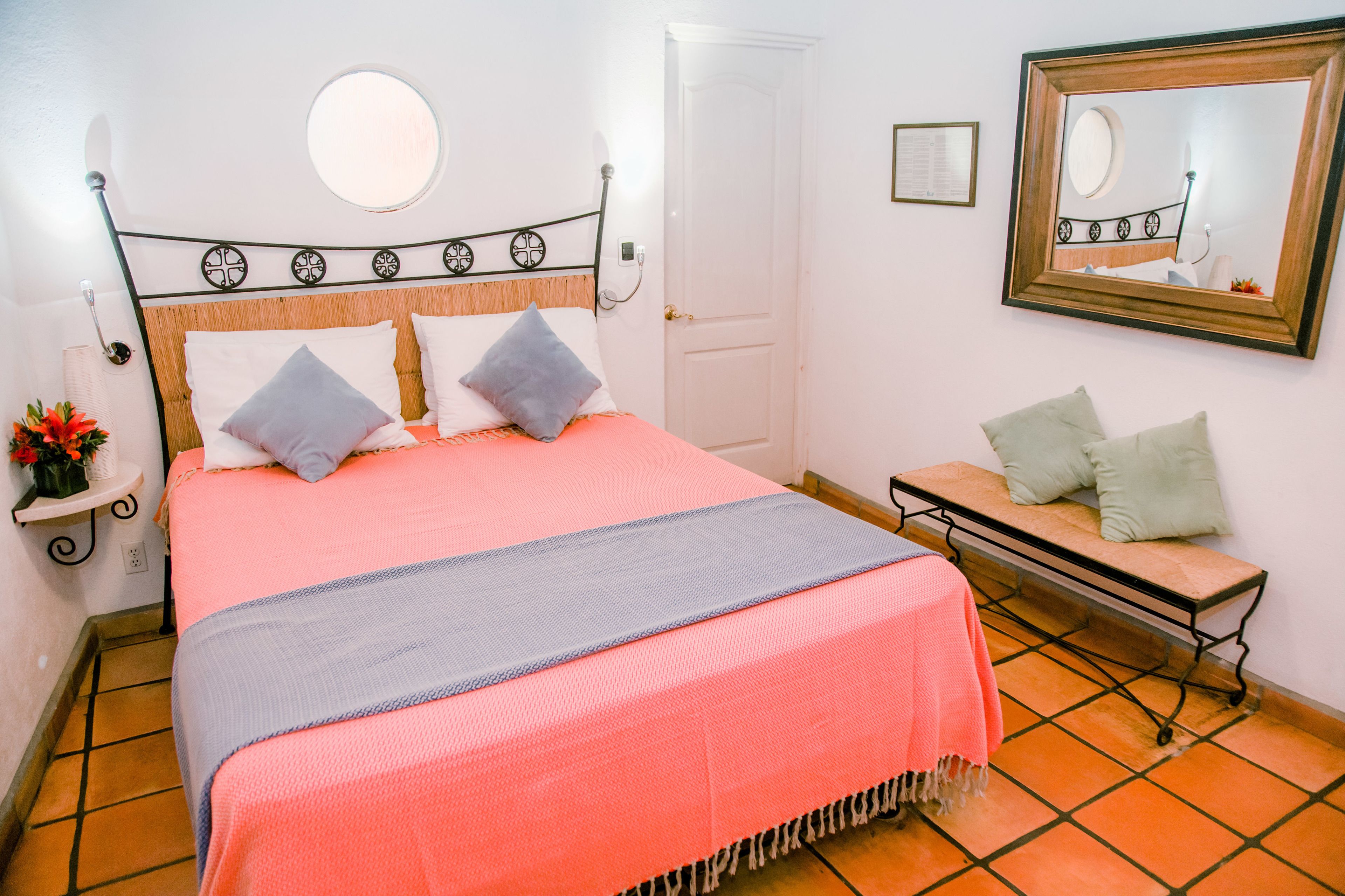 Un dormitorio con cama, mesita de noche, banco, espejo y puerta.