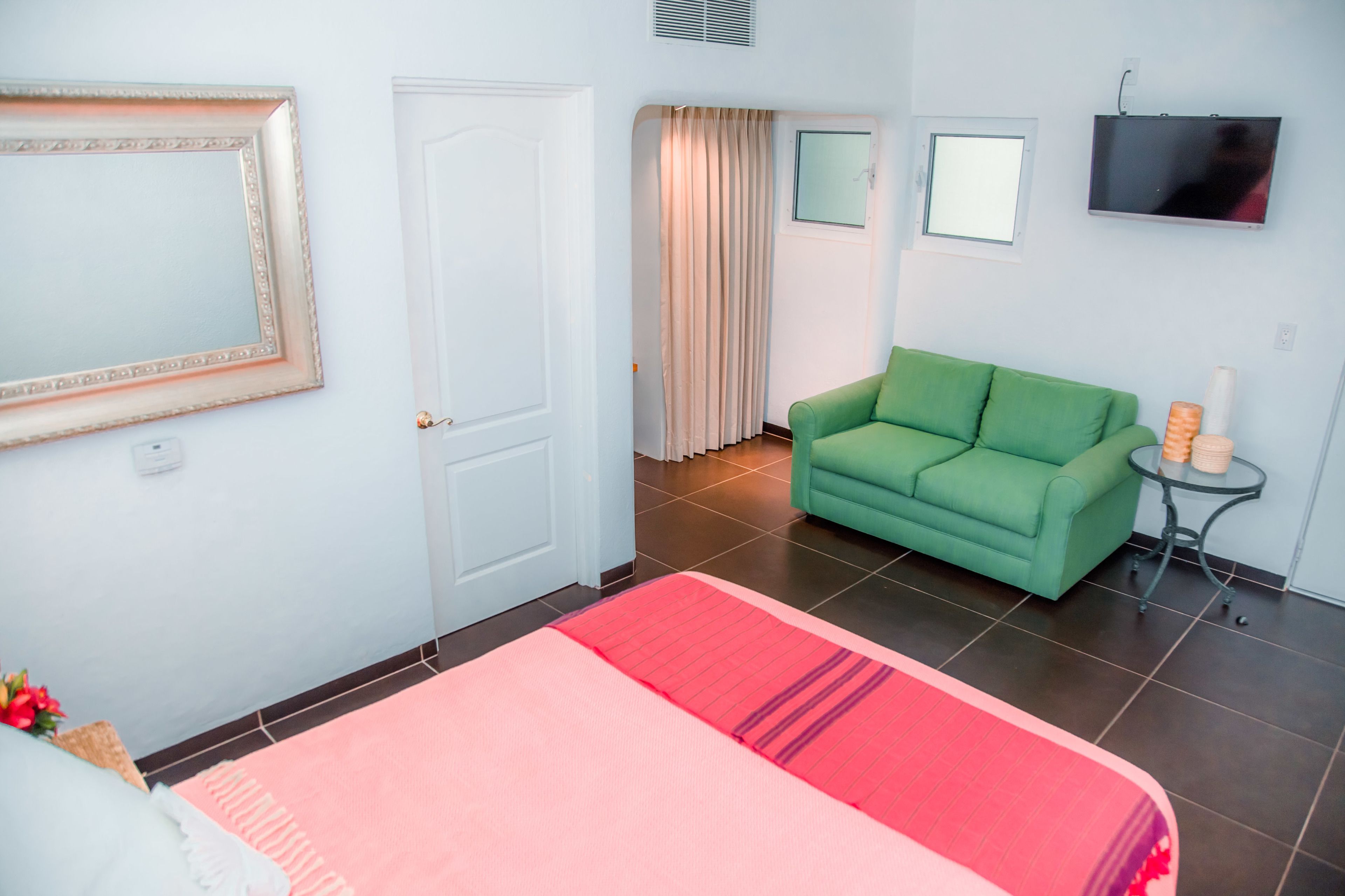 Ett hotellrum med en säng, en grön soffa, ett litet bord med en lampa, en tv och ett fönster med gardiner.