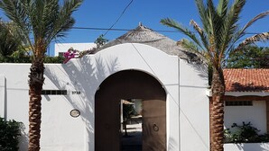 Un edificio bianco con tetto in tegole e un ingresso ad arco. Palme da entrambi i lati dell'ingresso.