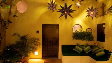 Une entrée chaleureuse, illuminée par des lampes en forme d’étoile, avec une porte, un banc agrémenté de coussins et des plantes en pot.