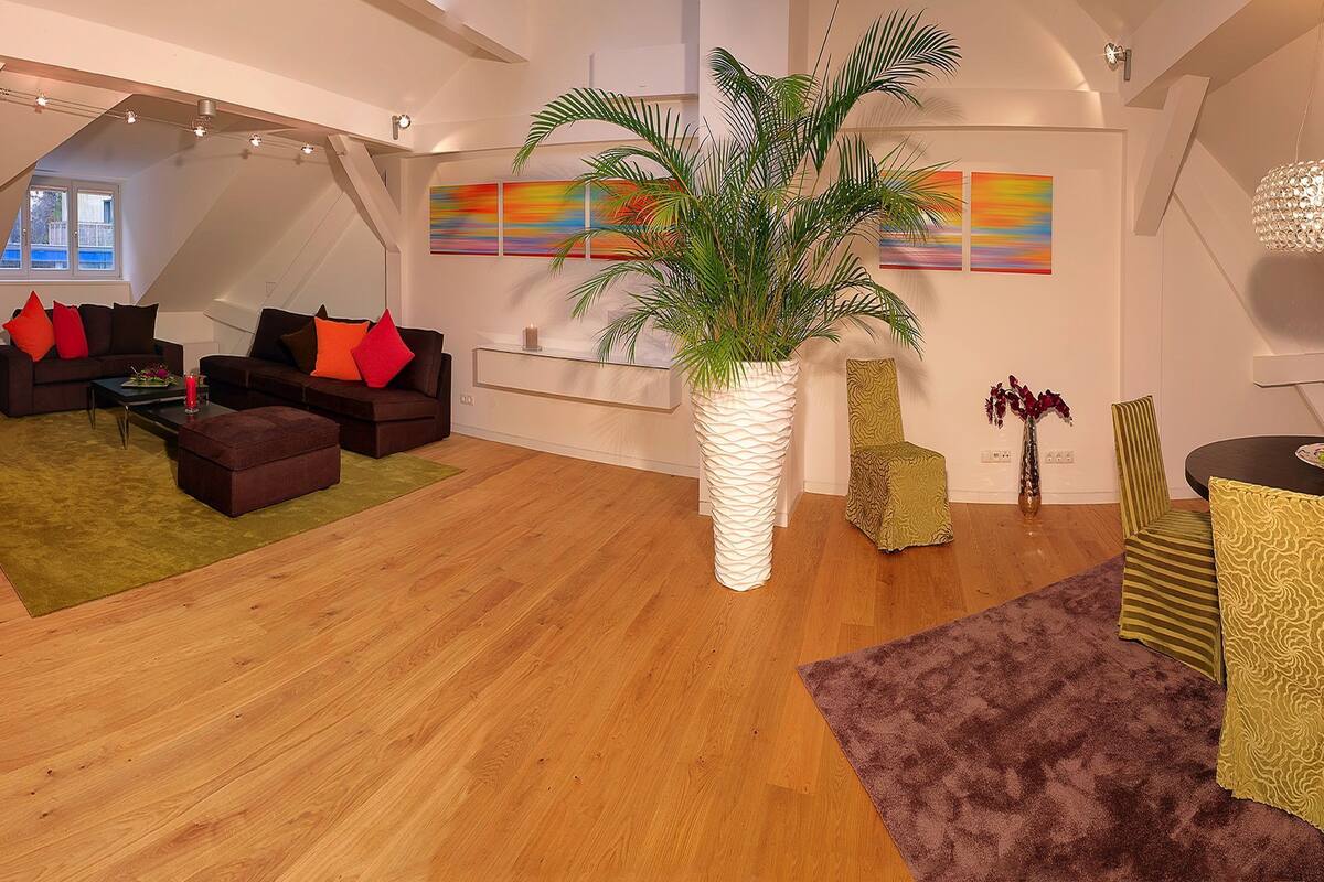 A spacious loft with a high ceiling, a dining area with a round table, and a living room with a large plant and modern furniture.