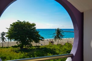 A beach view through a window with a view of the ocean, palm trees, and a wooden structure on the beach.