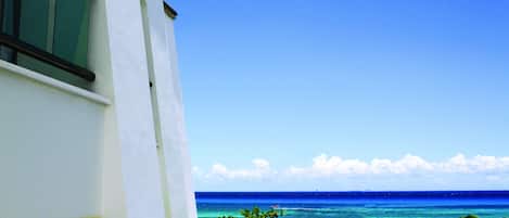 A view of a beach with clear blue water and a white building in the foreground.