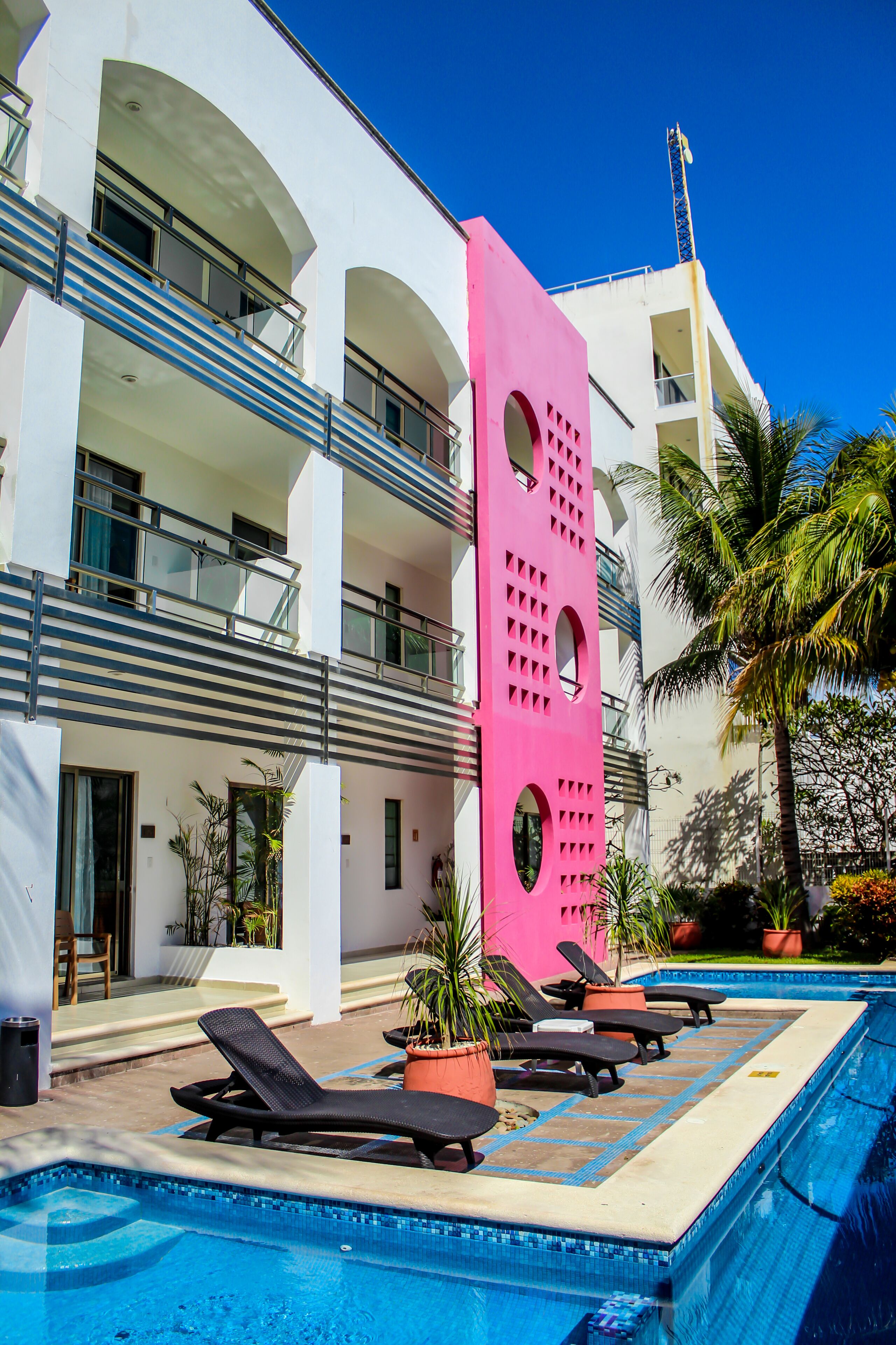 Um hotel moderno com área de piscina, espreguiçadeiras e uma estrutura rosa marcante.