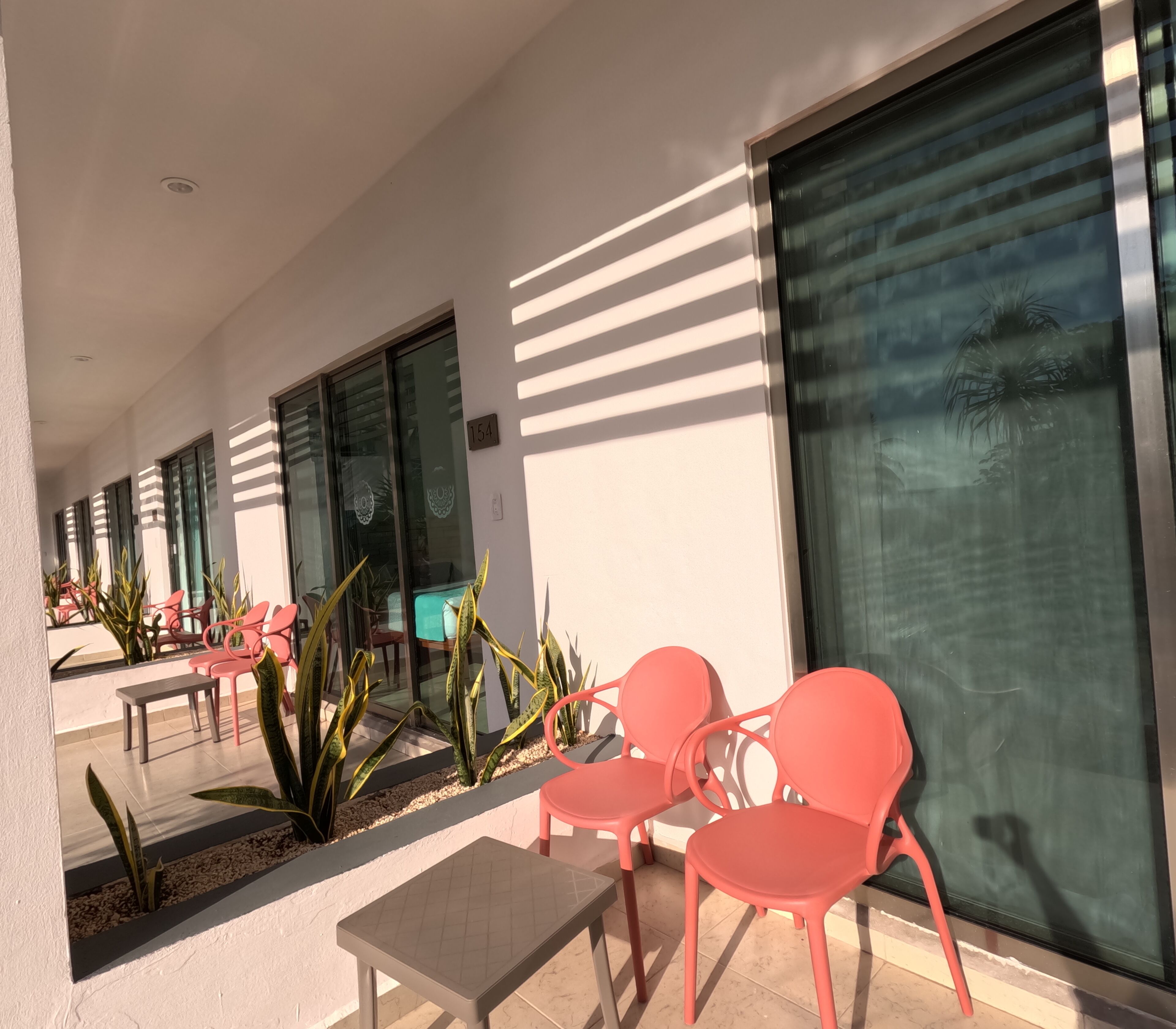 A modern outdoor seating area with red chairs and a table, large windows, and a number '154' sign.
