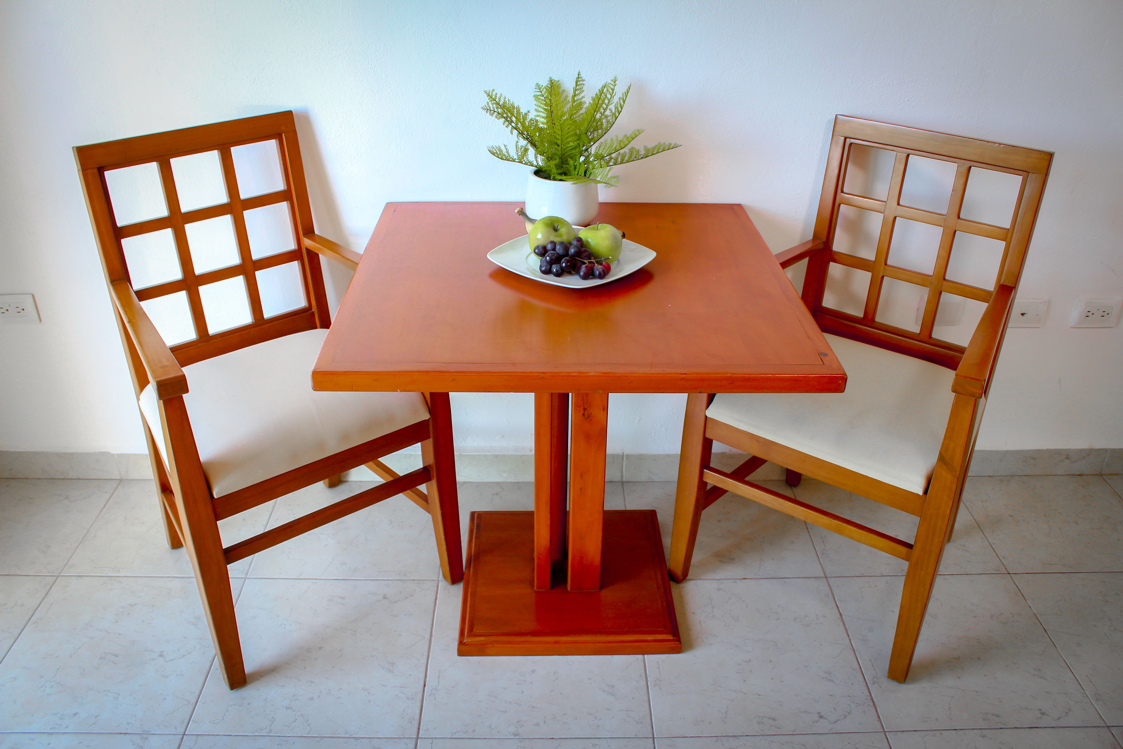 Una mesa de madera con un plato blanco de fruta y una planta en maceta.