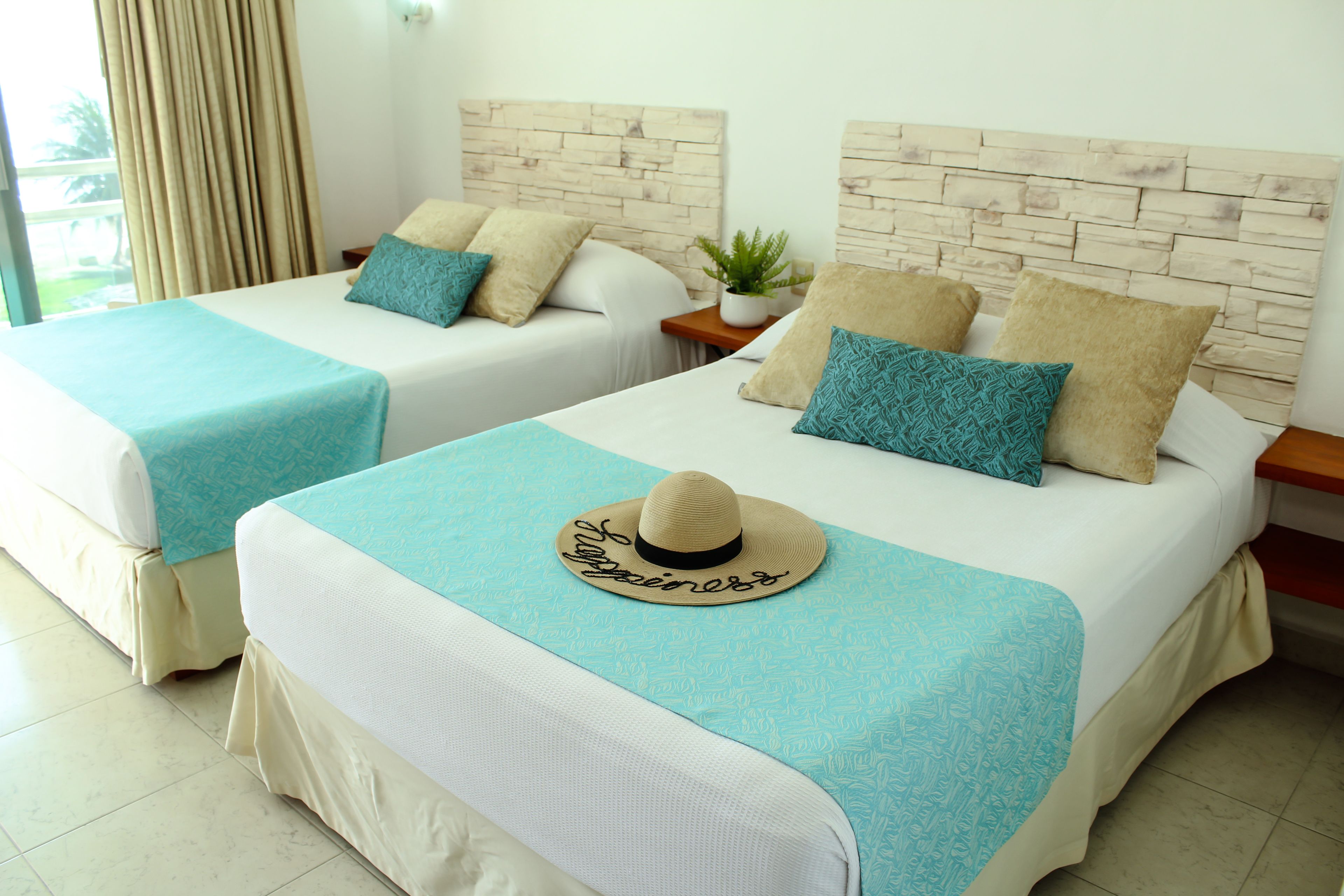 Two twin beds with matching headboards, a small potted plant, and a decorative hat on the bed.
