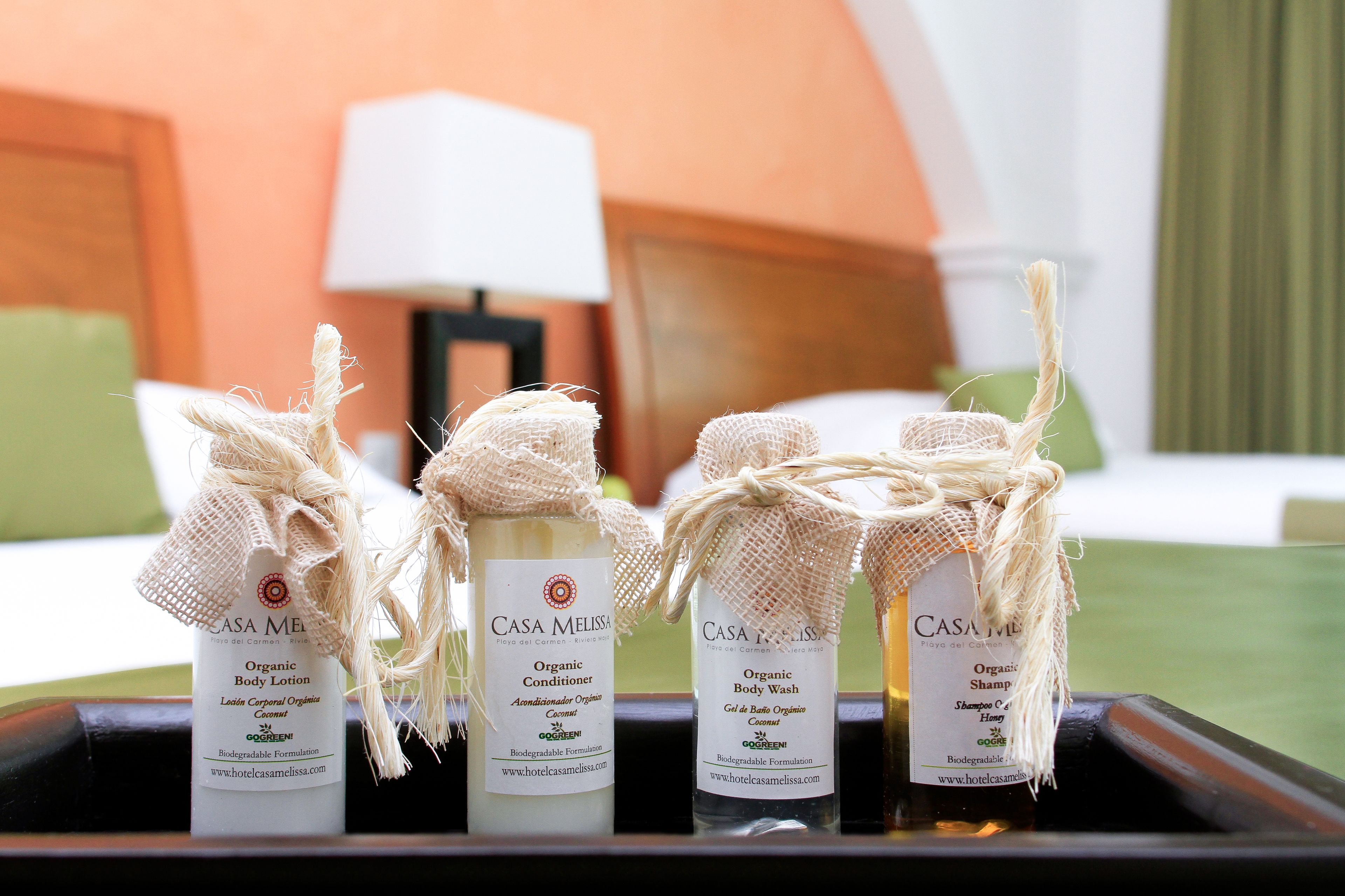 Una bandeja con cuatro botellas de productos orgánicos para el cuidado corporal de Casa Melissa, que incluyen loción corporal, acondicionador, jabón de baño y champú, cada uno con una etiqueta de arpillera.