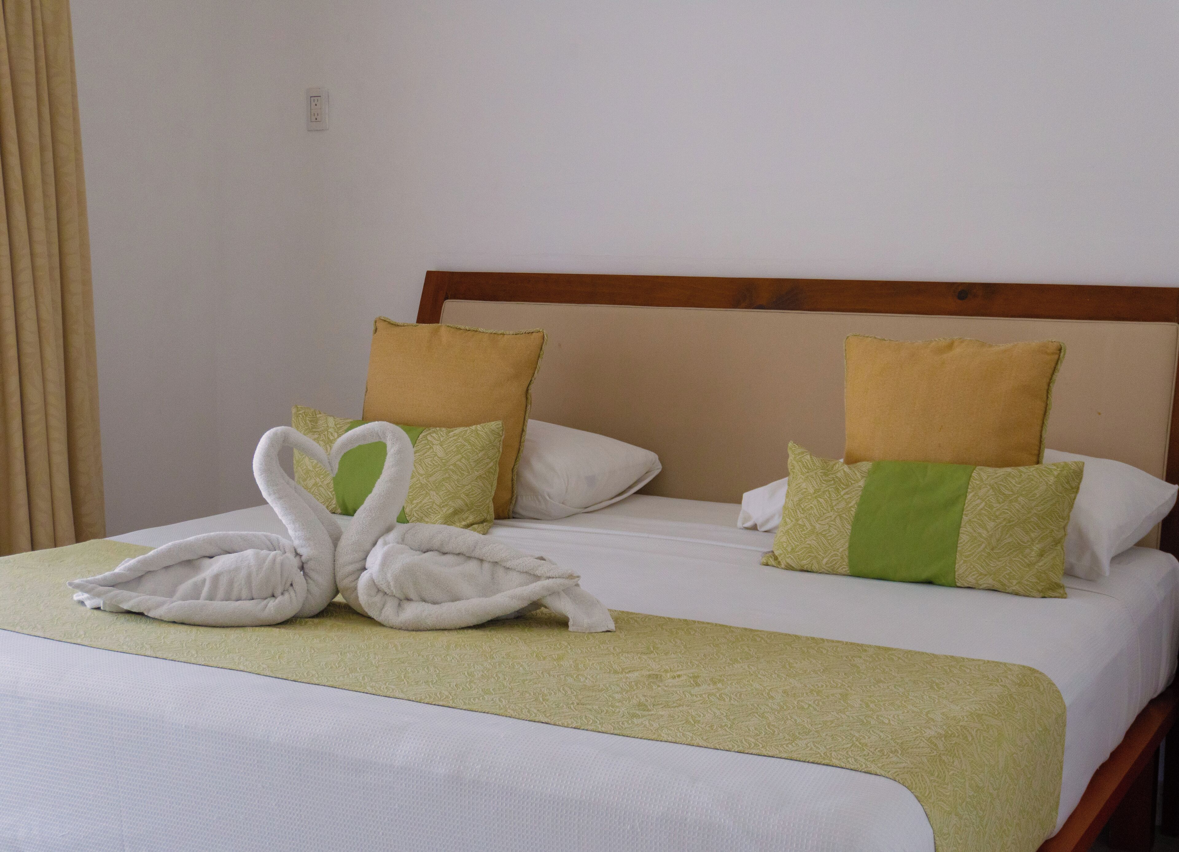 Een hotelkamer met een bed, twee kussens, een deken en een handdoek, gevouwen in de vorm van zwanen.