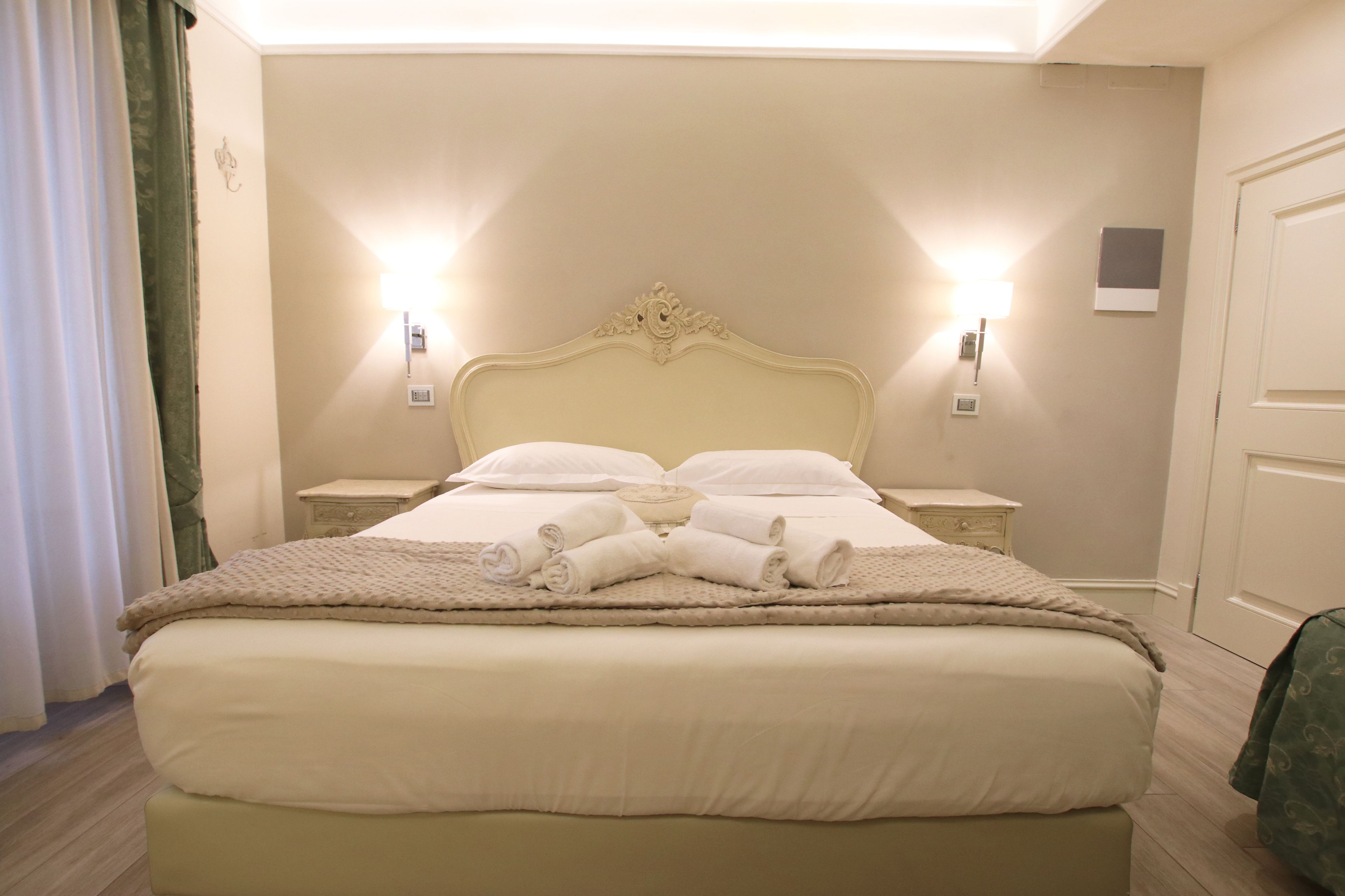 A neatly made bed with white linens and towels, two bedside tables with lamps, and a door to the right.