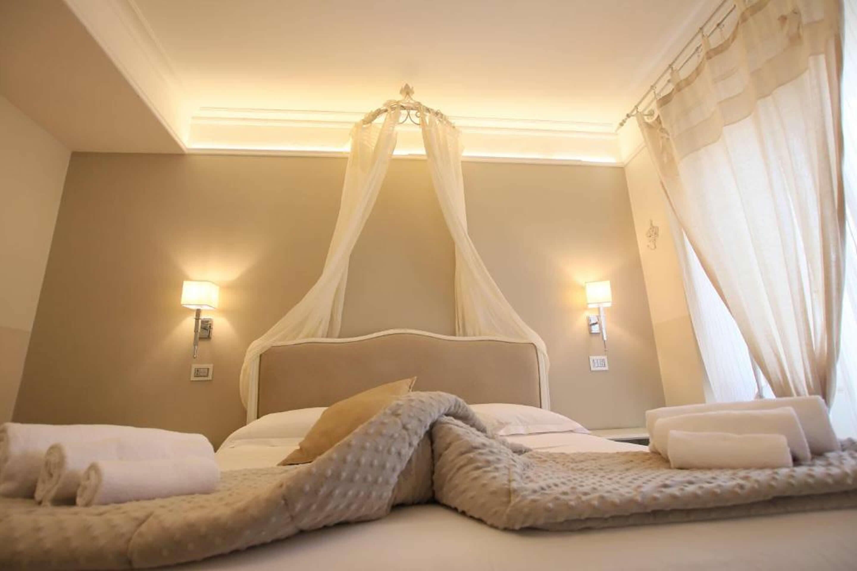 Une chambre d’hôtel avec un lit à baldaquin, deux lampes de chevet et une décoration aux couleurs neutres.