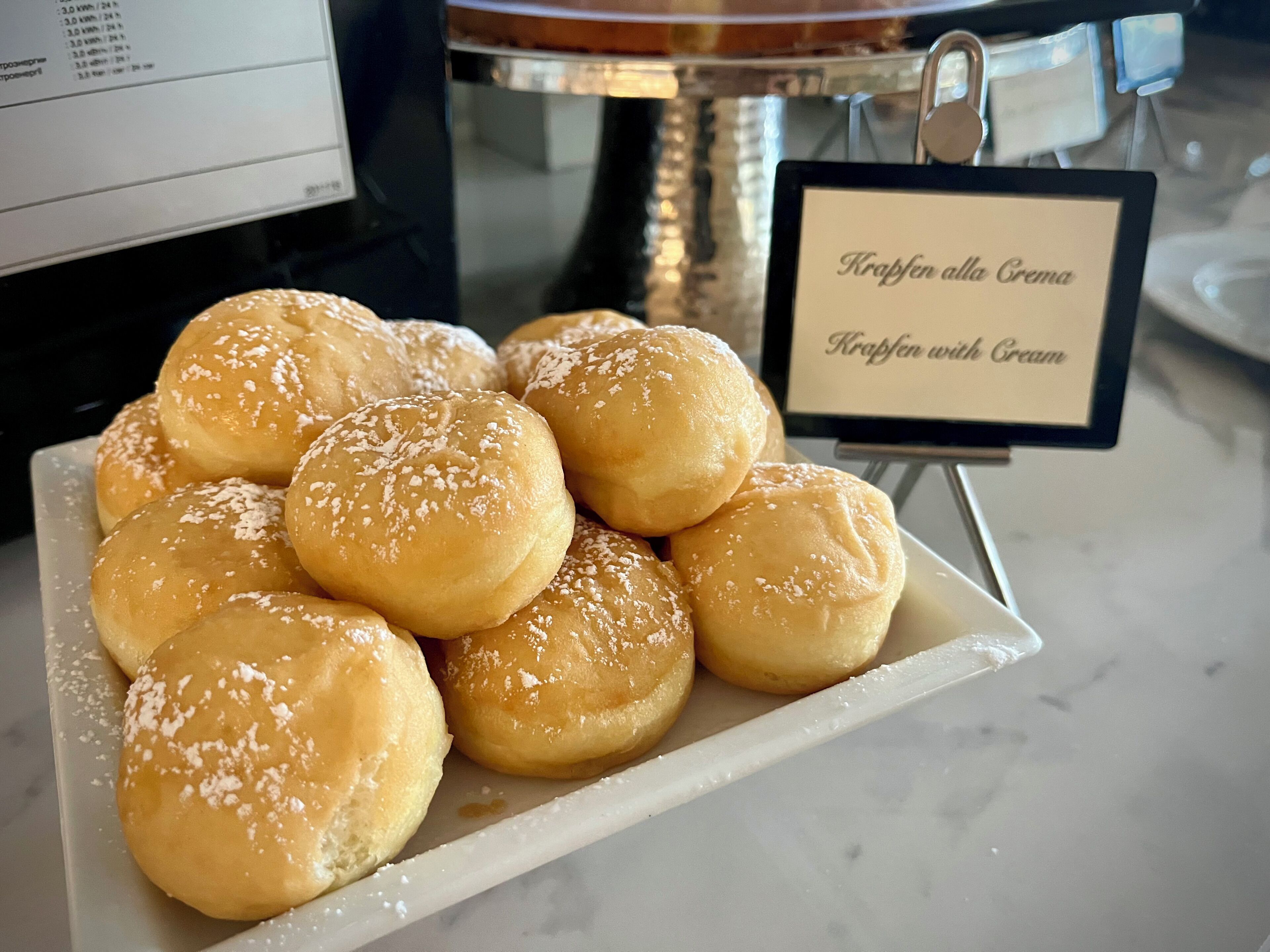 Een schaal met roomgevulde broodjes, met een bordje met de tekst 'Krapfen alla Crema'.