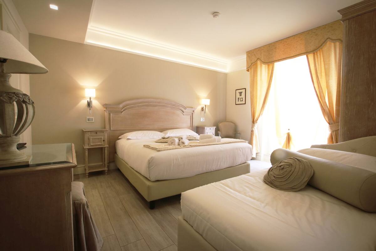 A hotel room with a large bed, two bedside tables, a lamp, and a view of the outdoors.