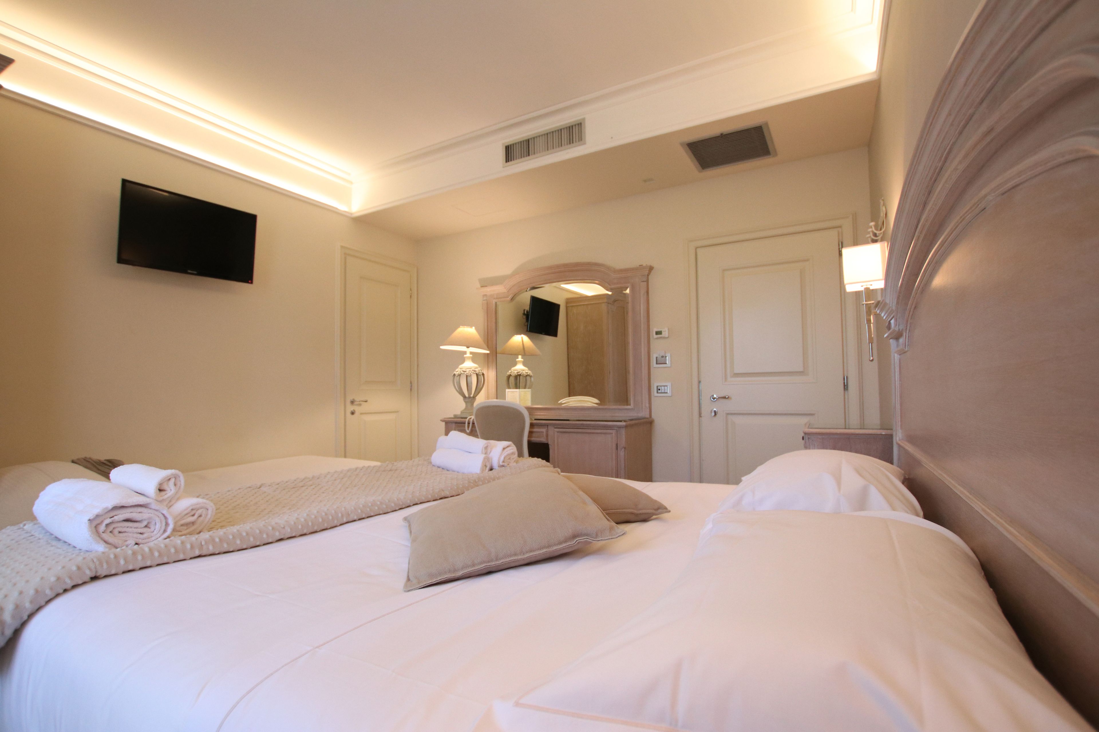 Una habitación de hotel con una cama grande, un televisor montado en la pared, un escritorio con lámpara y un espejo sobre otro espejo.