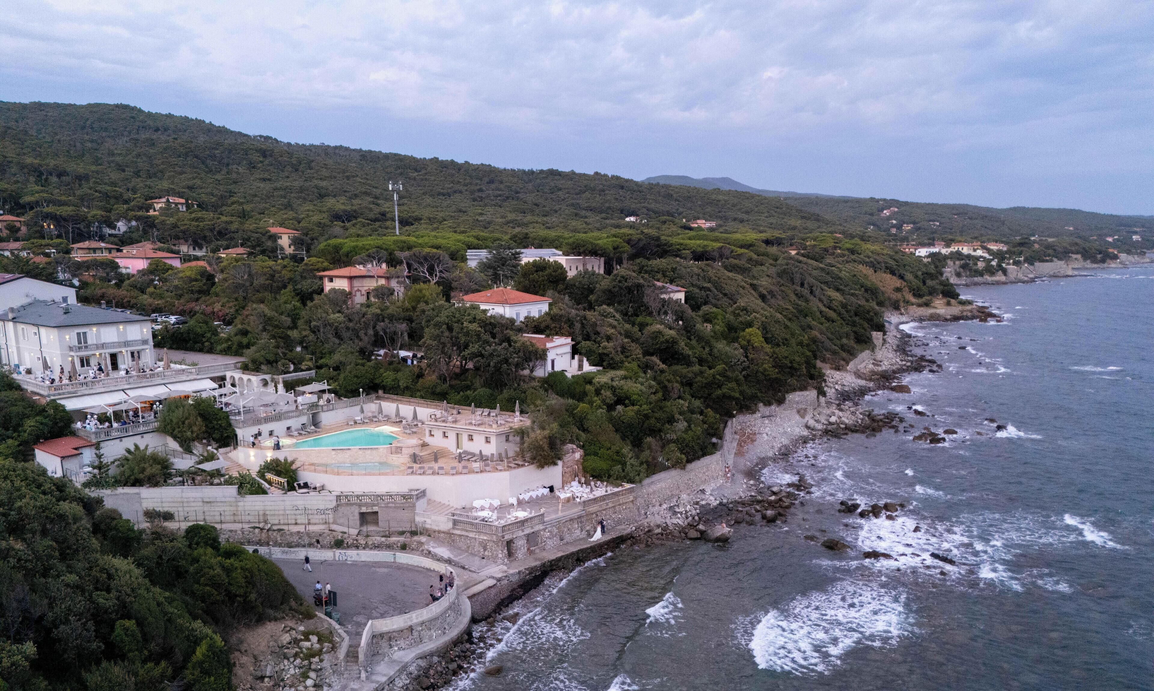 Vista aérea de una propiedad costera con piscina, un muro de contención de piedra y una playa.