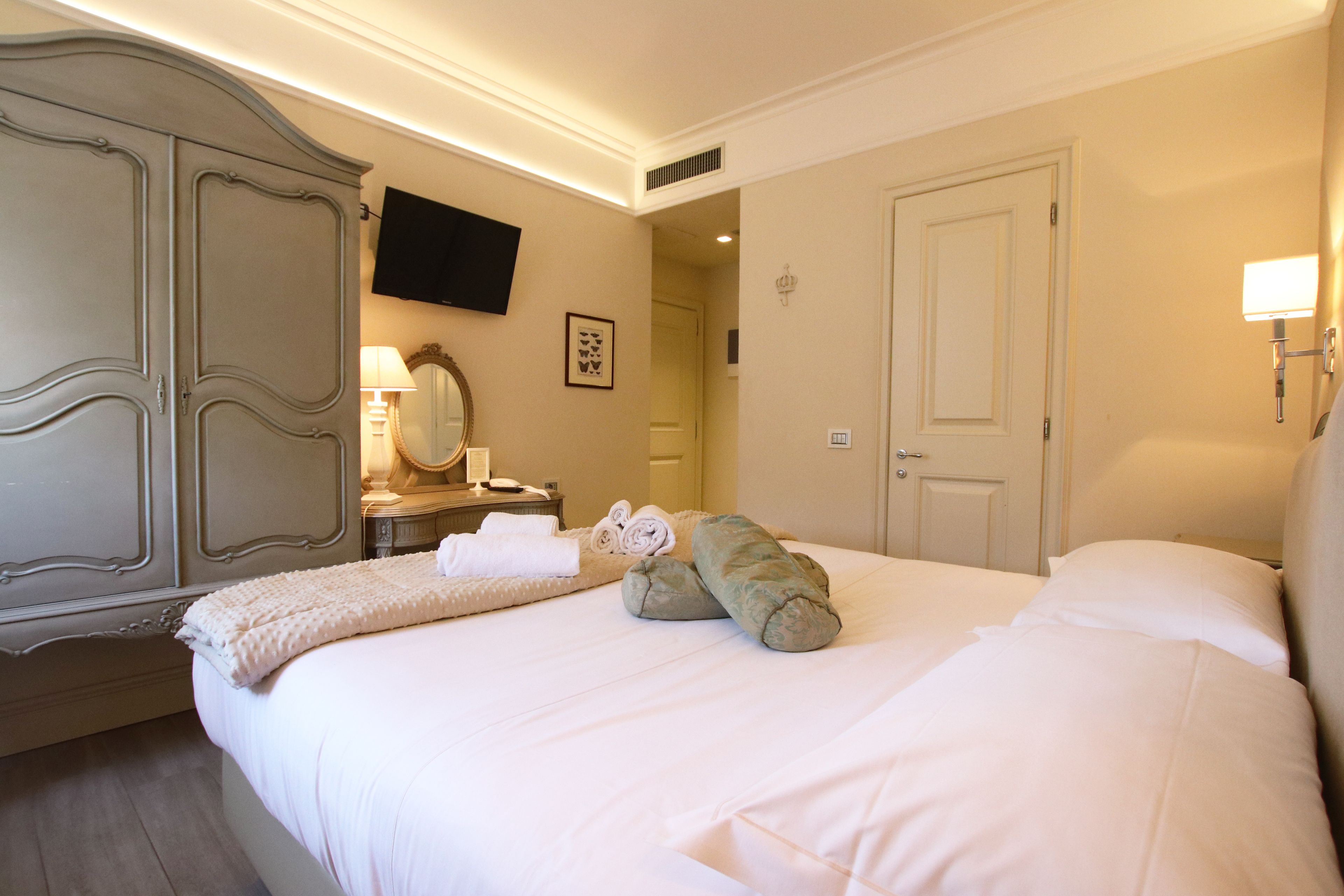 A hotel room with a large bed, a wardrobe, a flat-screen TV mounted on the wall, and a bedside lamp.